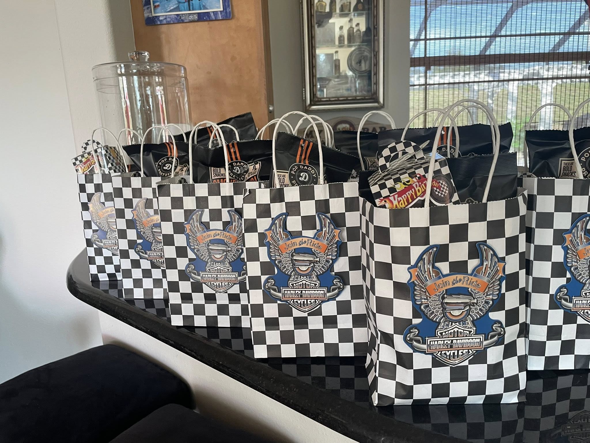 Row of Harley-Davidson themed party favor bags with checkerboard patterns and wing logos lined up on a counter.