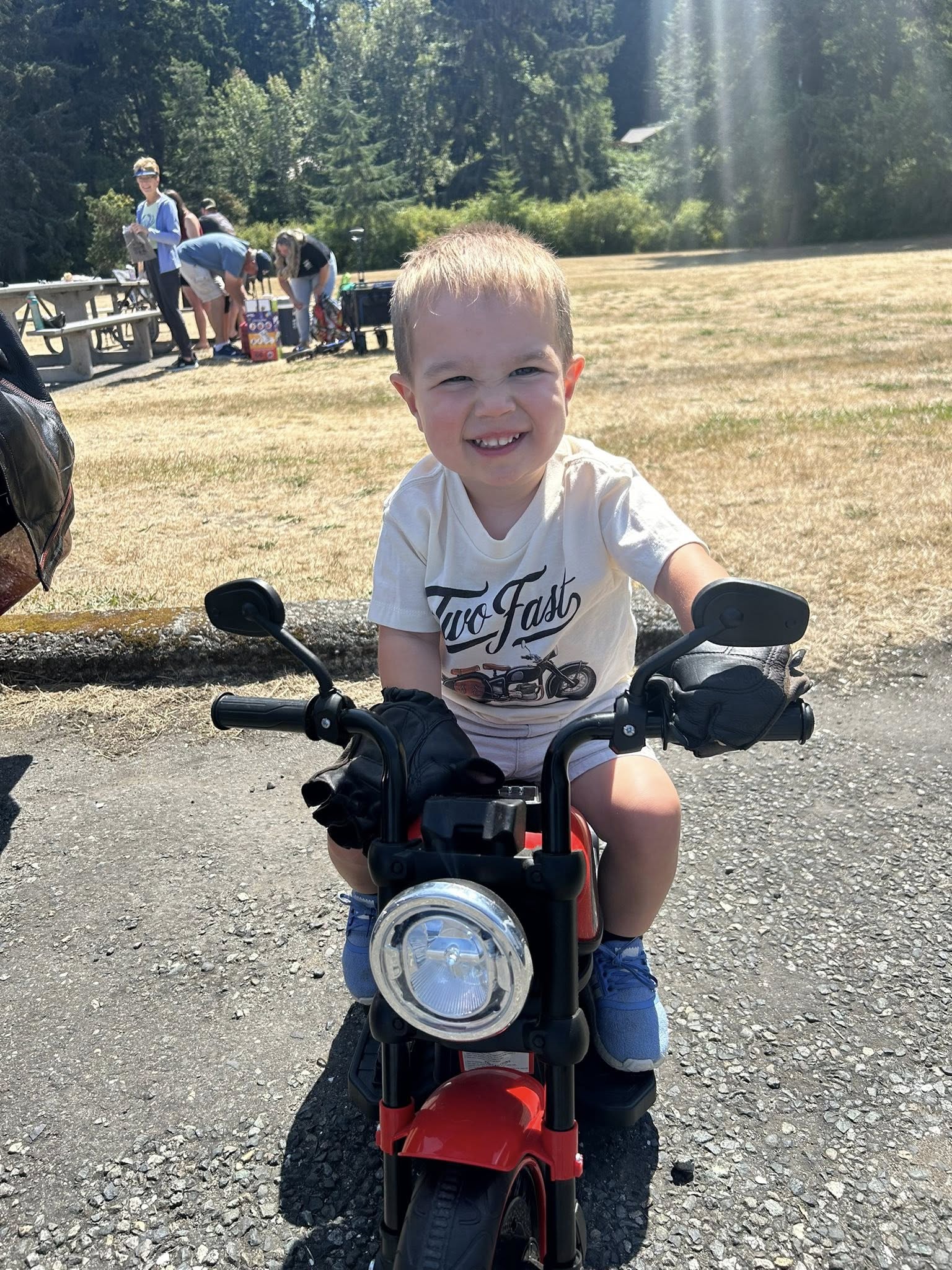 Toddler smiling while sitting on a toy red motorcycle at a park