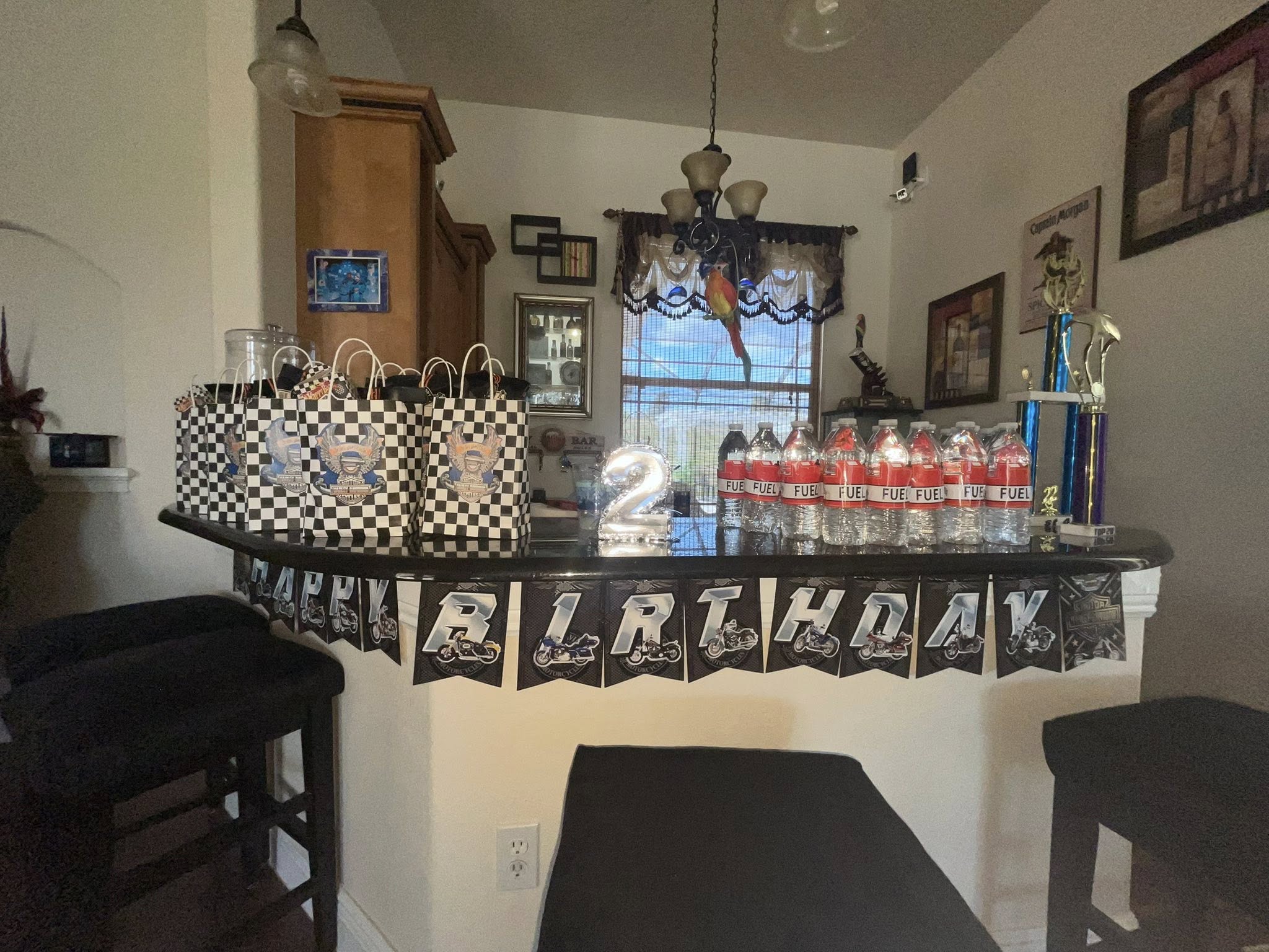 Motorcycle-themed second birthday party decorations on a home bar counter with checkered gift bags and fuel bottles