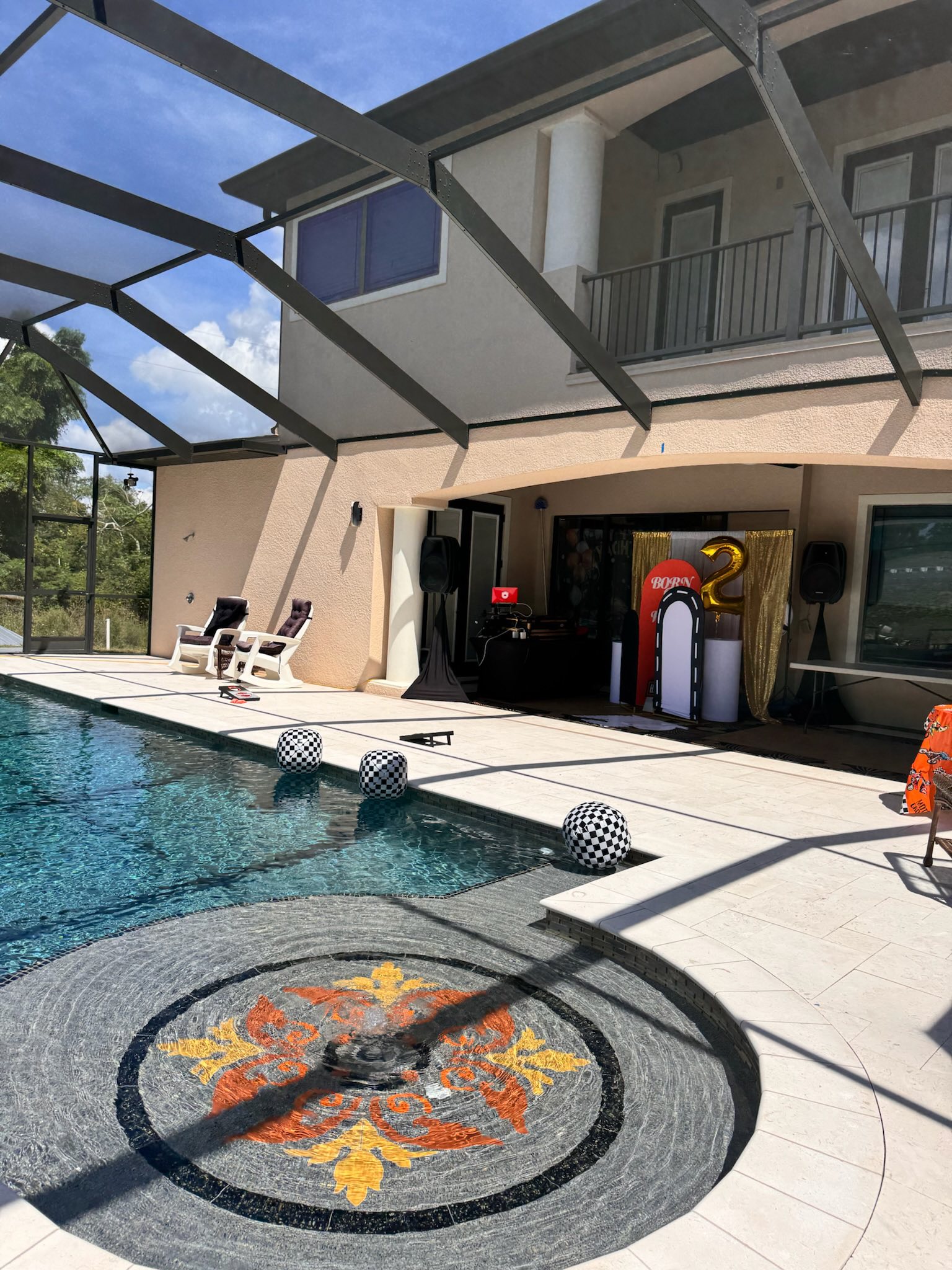Patio deck decorated for a child's birthday party with race car-themed signage and number 2 balloon near a pool.