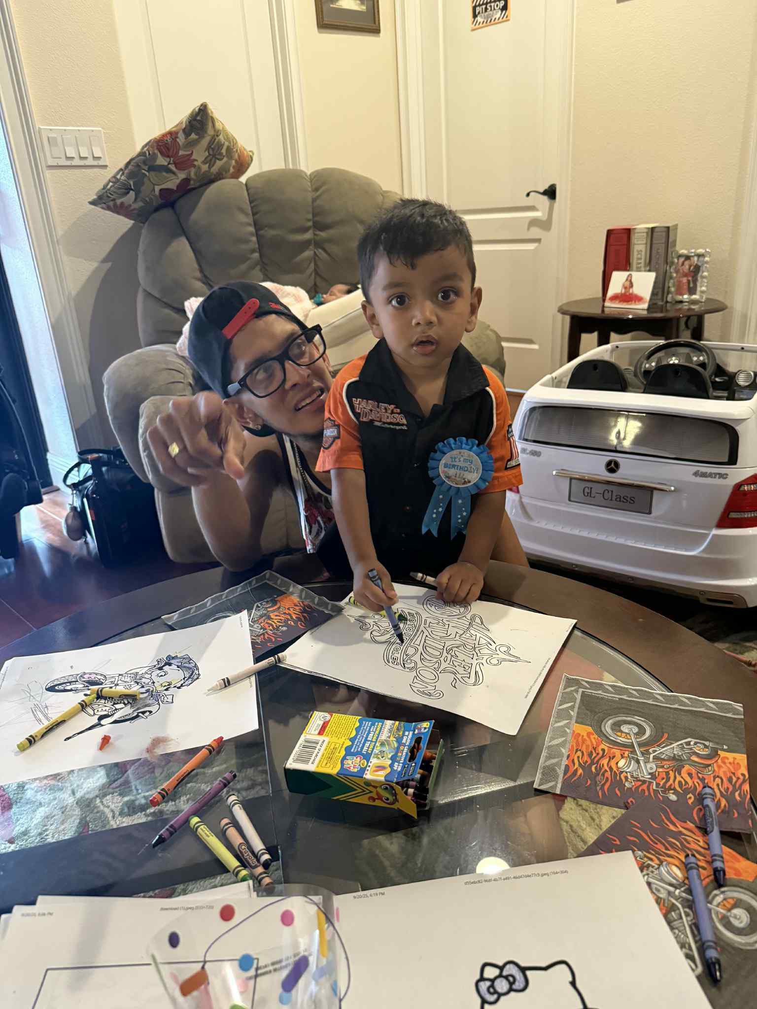 Toddler wearing a birthday badge coloring a Harley-Davidson-themed page alongside an adult.