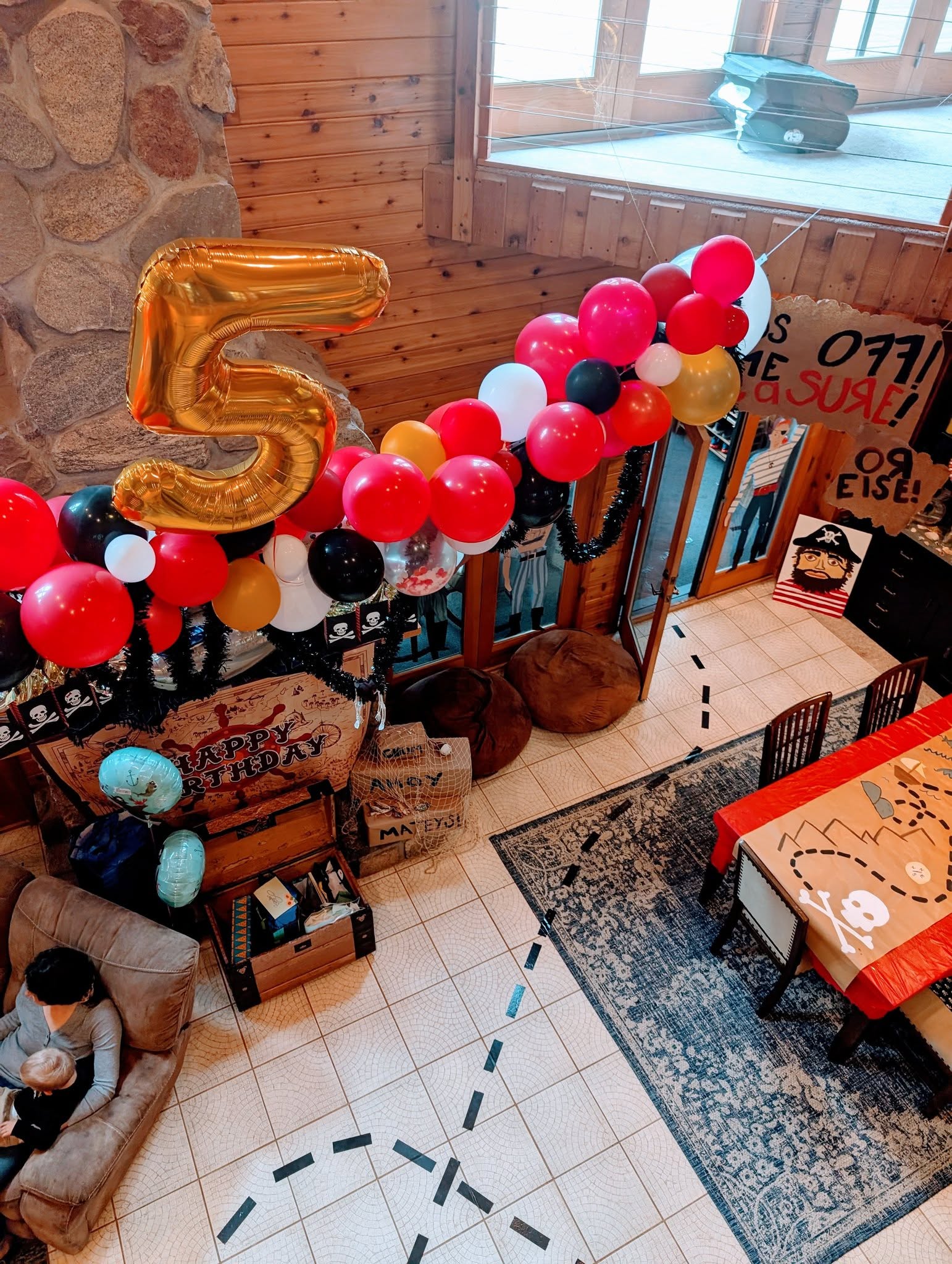 A pirate-themed fifth birthday party setup with a giant gold 5 balloon, a balloon garland, and a treasure map table.