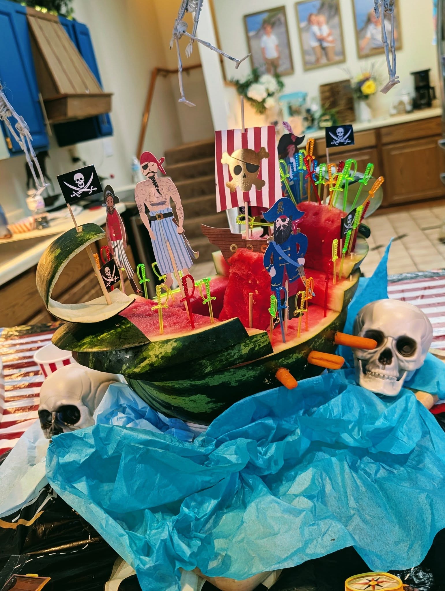 A creative watermelon carved into a pirate ship decorated with paper pirates, flags, and colorful sword picks.