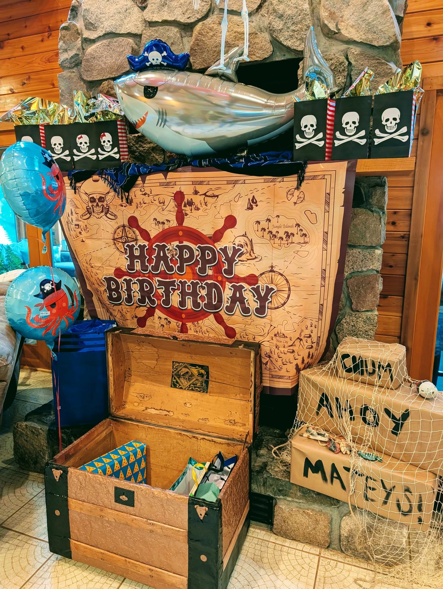Pirate-themed birthday party decorations featuring a Happy Birthday treasure map banner, shark and octopus balloons, and a wooden chest.