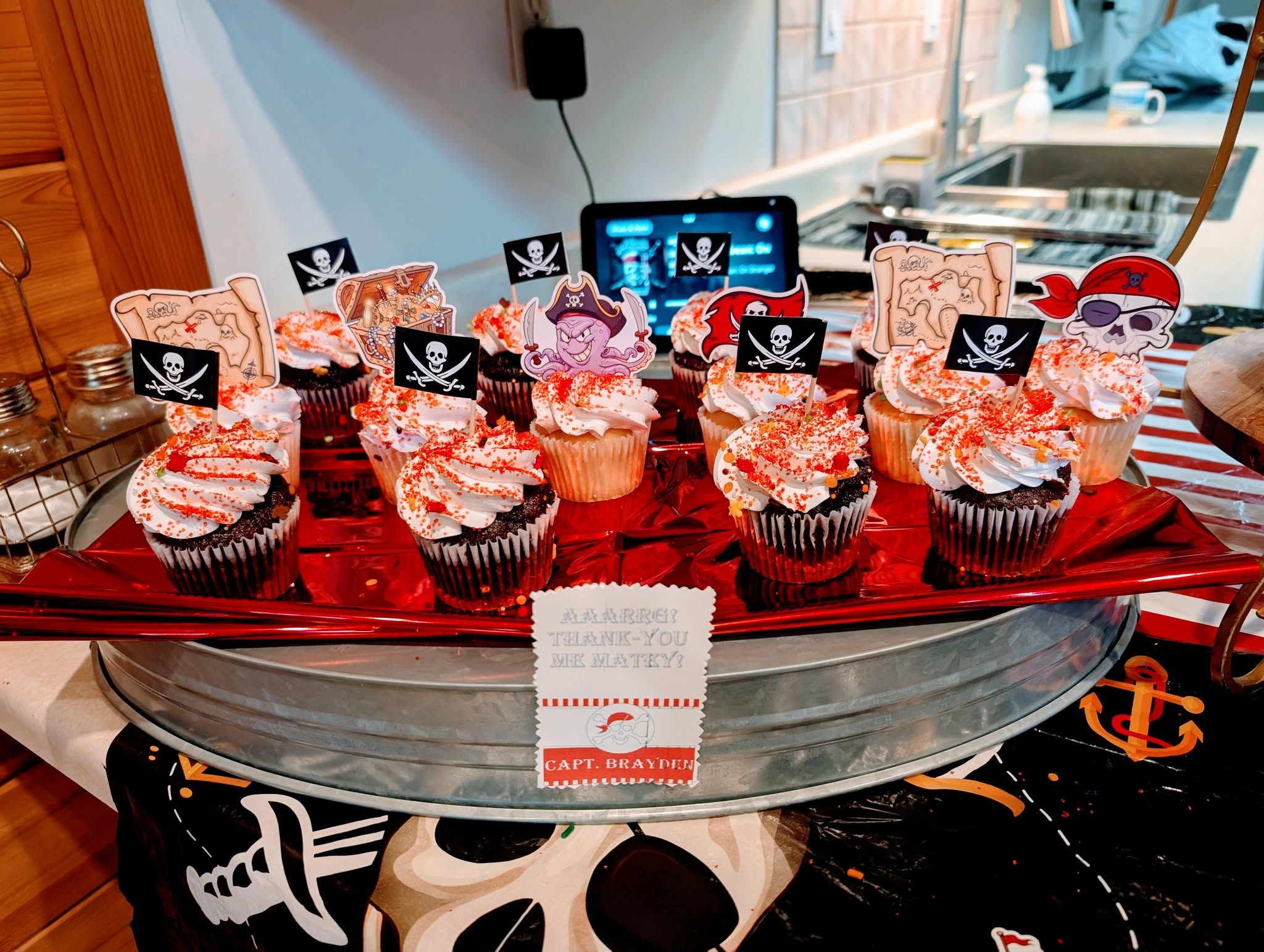 Table display of chocolate cupcakes decorated with pirate-themed toppers and a thank you sign for a party.