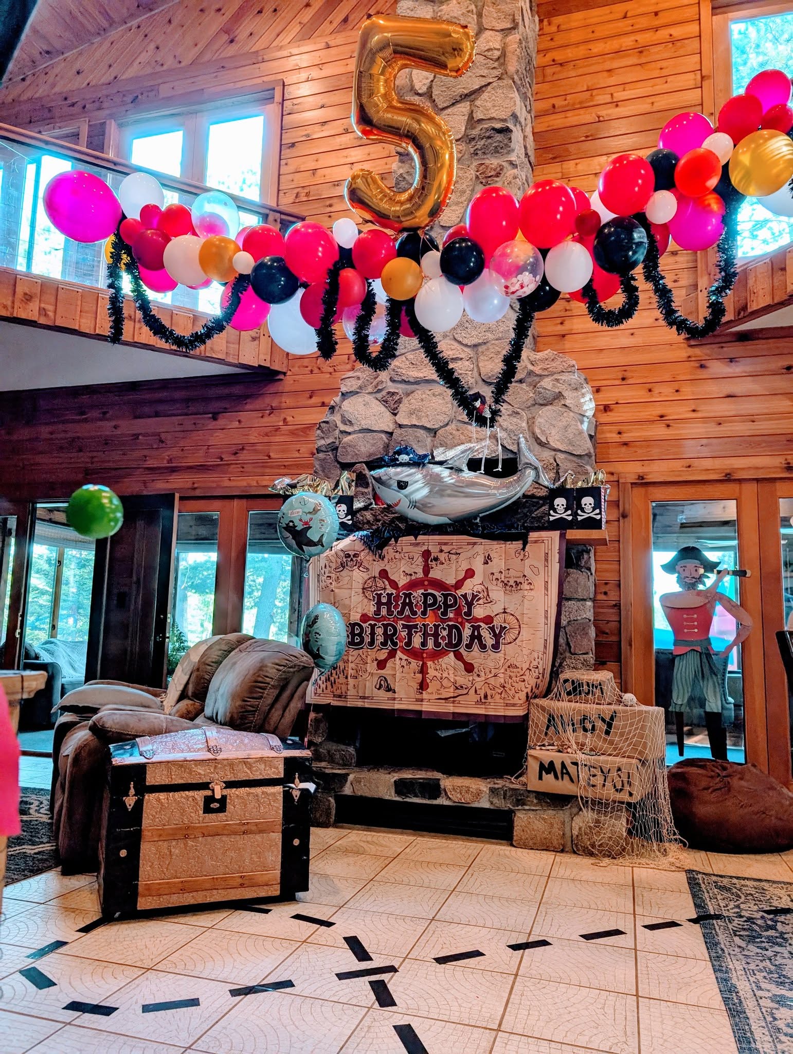 Pirate-themed birthday decorations for a 5th birthday featuring a gold balloon number 5 and a treasure chest.