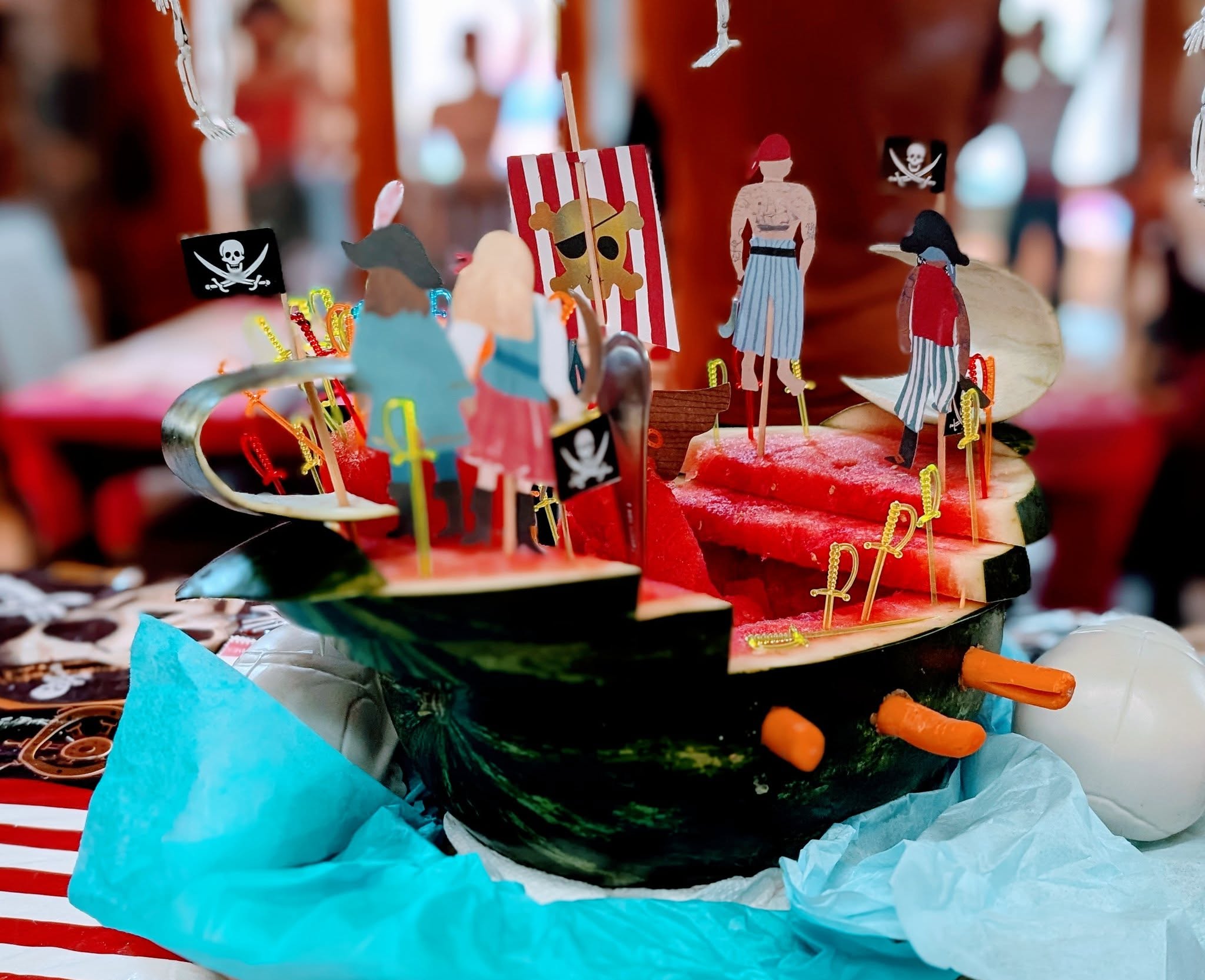 Carved watermelon pirate ship centerpiece with pirate flag and character decorations.