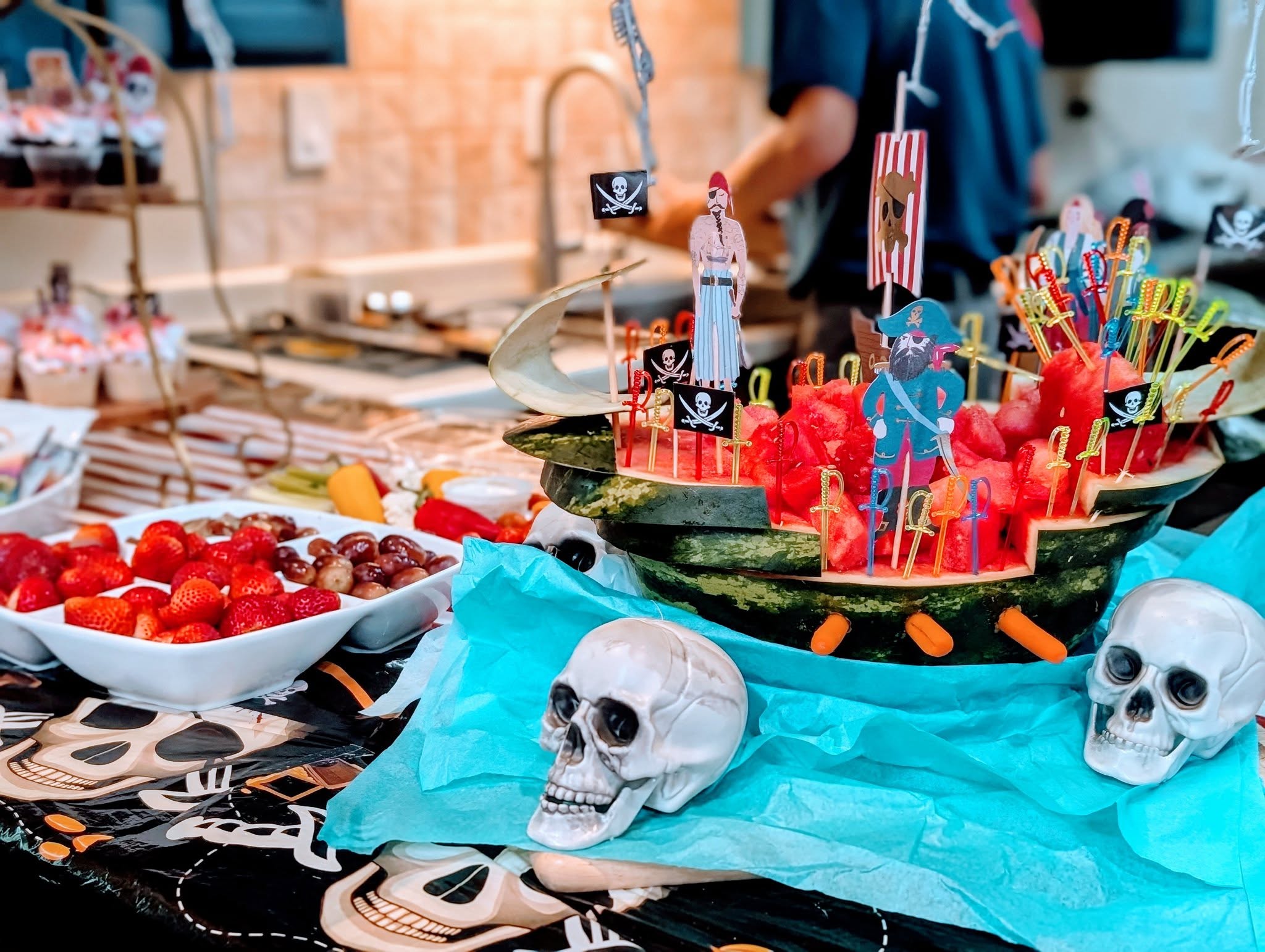Watermelon carved as a pirate ship decorated with skull figures for a themed party.