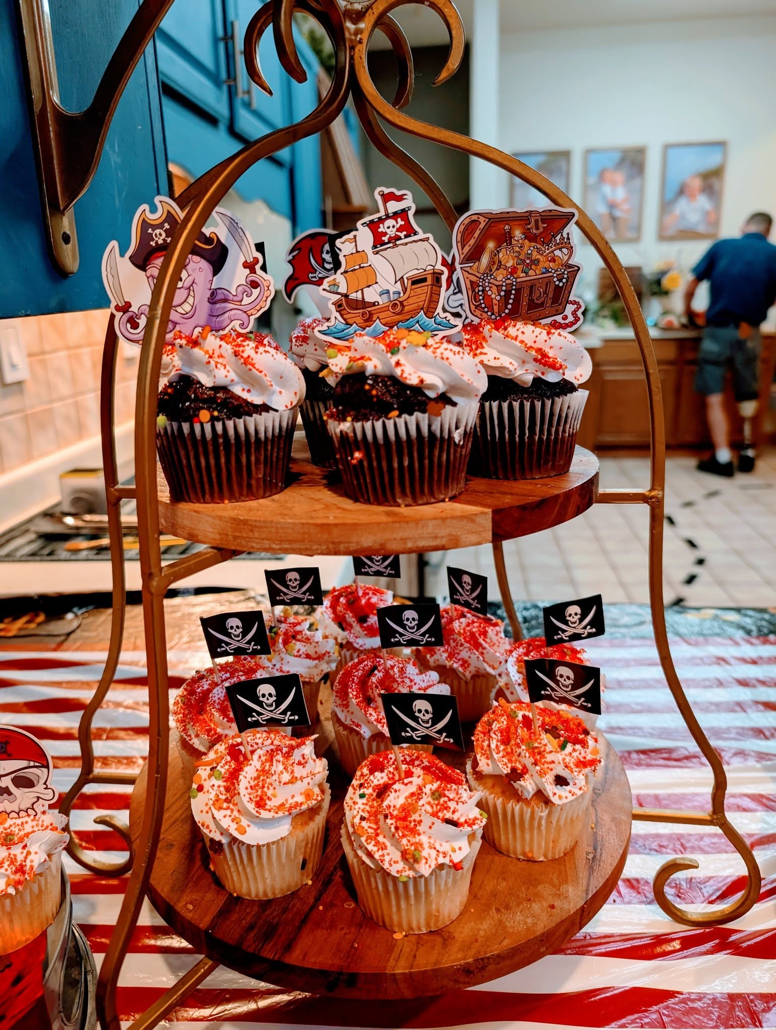 Two-tiered dessert stand filled with pirate-themed cupcakes featuring skull-and-crossbones toppers and colorful sprinkles.