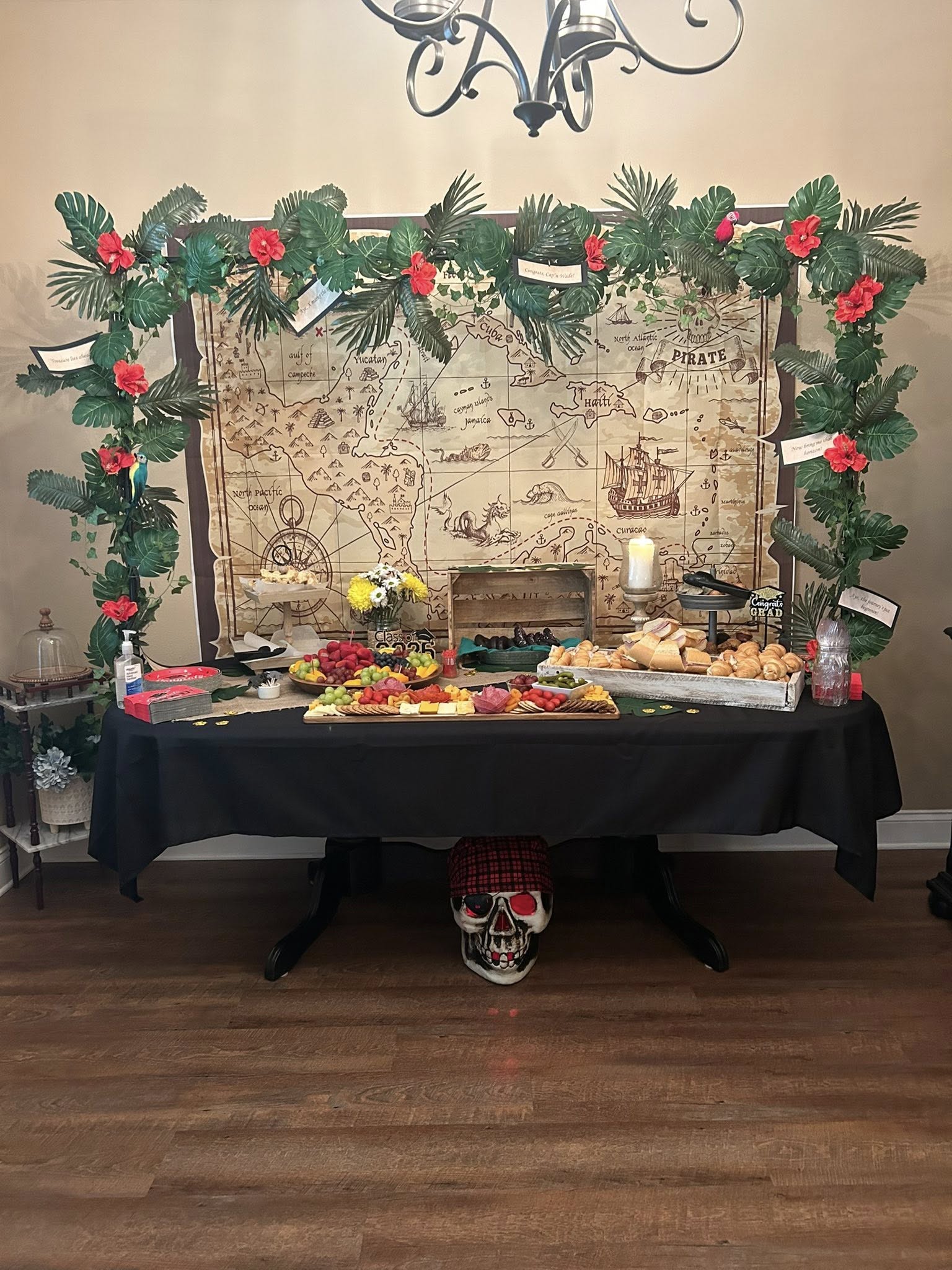 Pirate-themed food table featuring a treasure map backdrop, tropical greenery, and fruit and charcuterie boards.