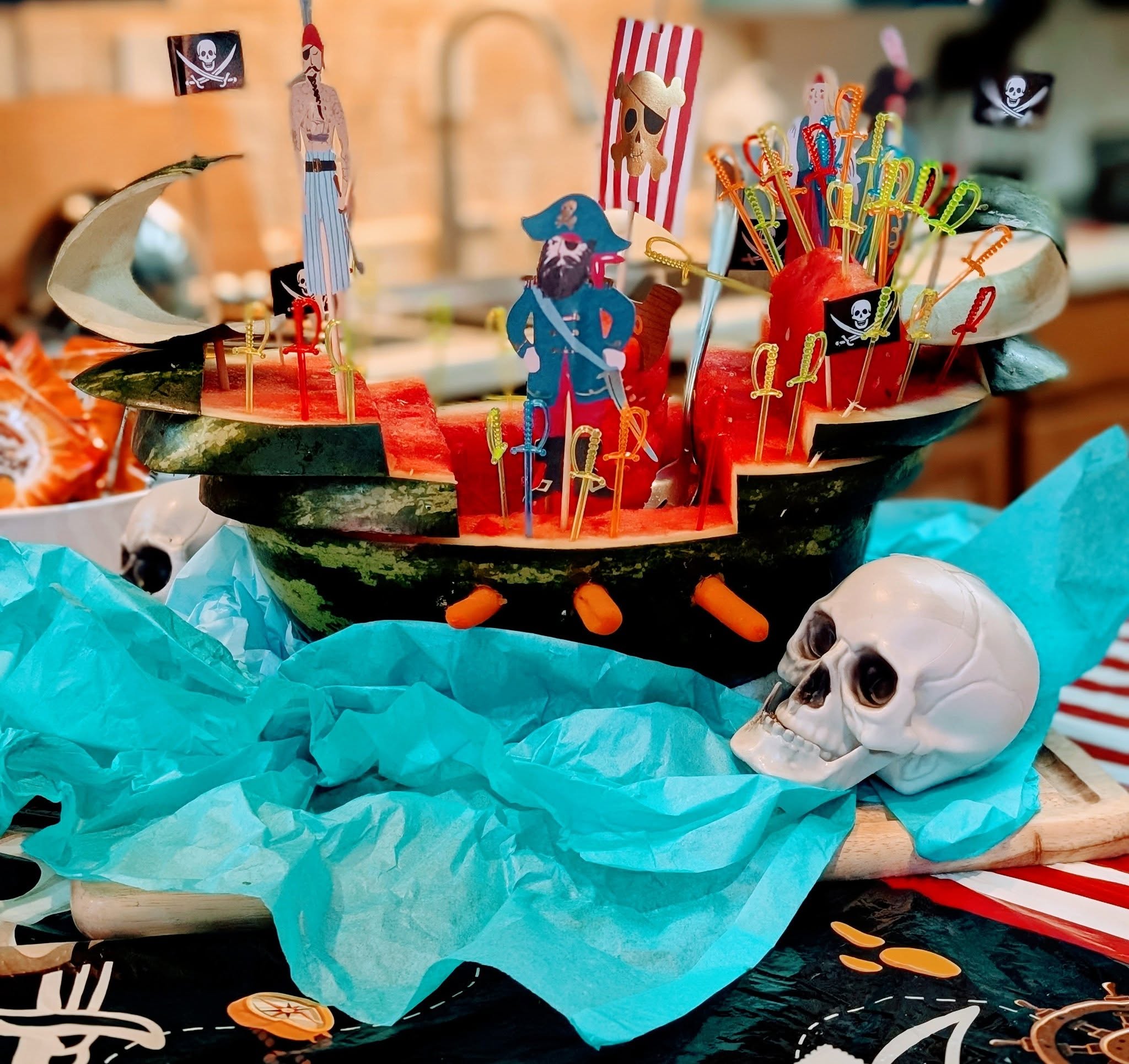 Carved watermelon pirate ship centerpiece with skull and sword decorations for a party