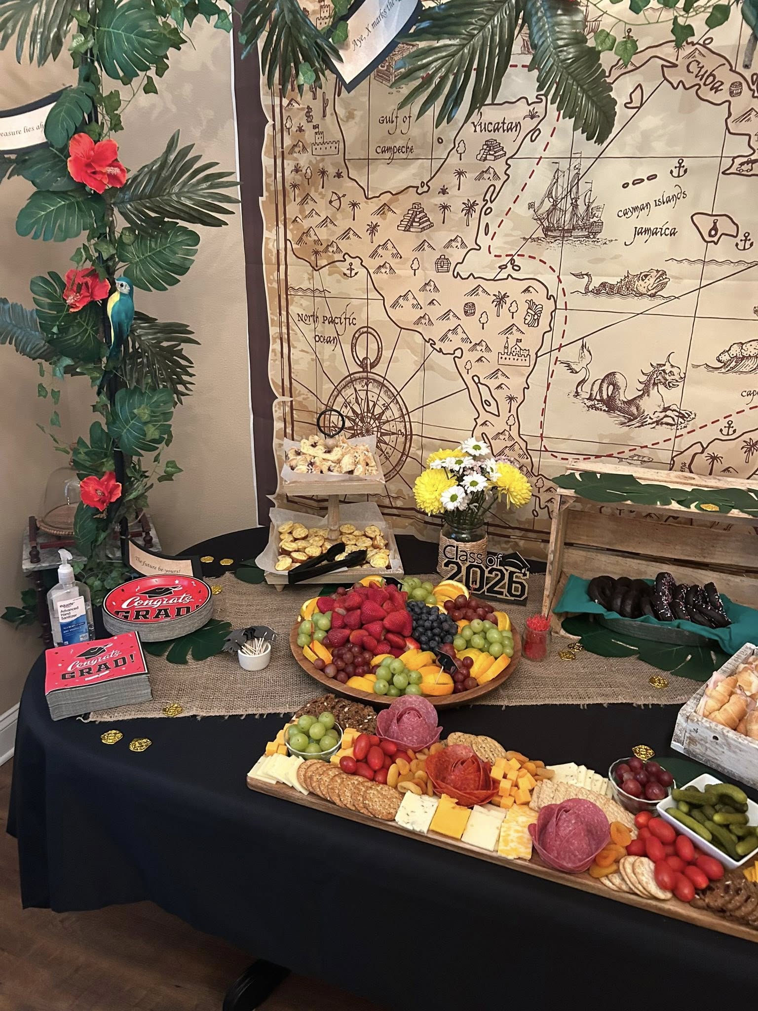 Table spread for a Class of 2026 graduation party with a pirate treasure map backdrop, snacks, and fruit.
