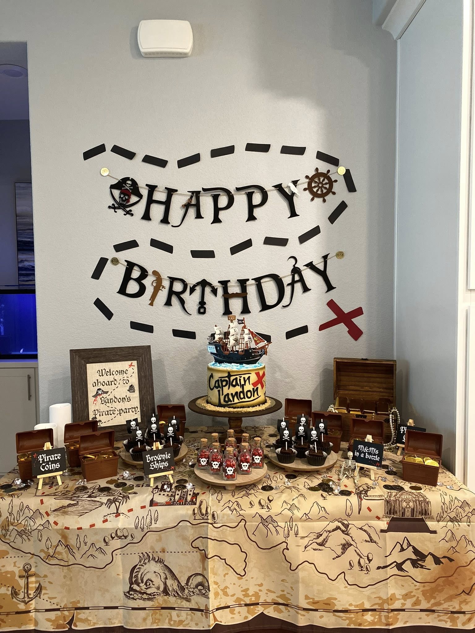 Pirate-themed birthday dessert table featuring a Captain Landon cake, brownie ships, and treasure chests.