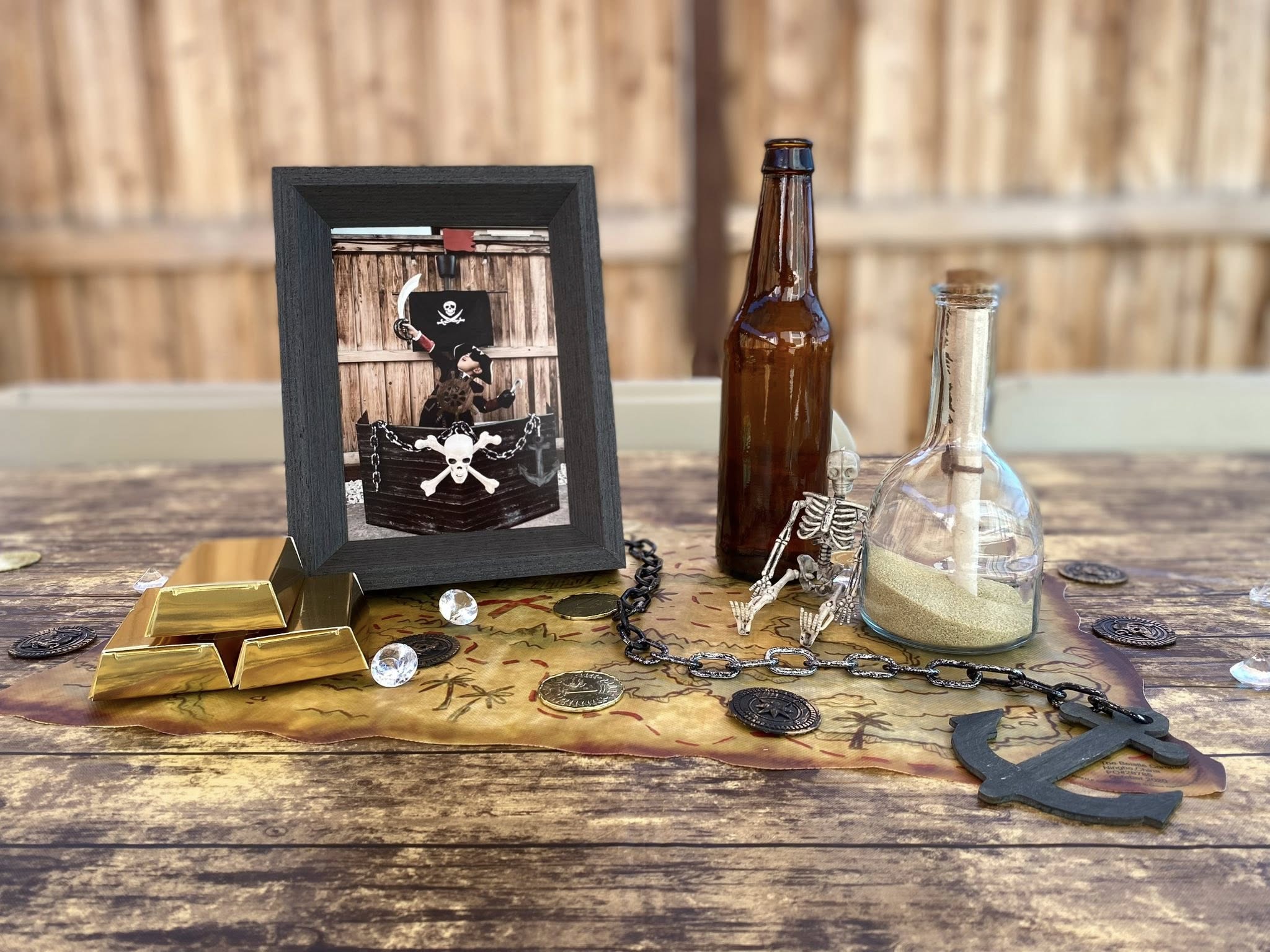 Pirate-themed table centerpiece with gold bars, plastic coins, a message in a bottle, and a framed pirate cutout.