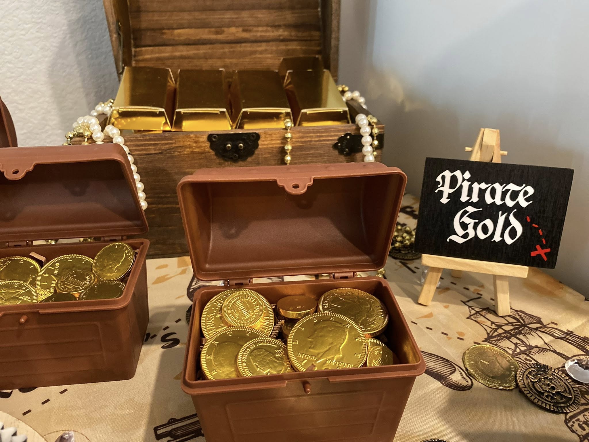 Tabletop display with small plastic treasure chests filled with gold coins and a sign labeled Pirate Gold.