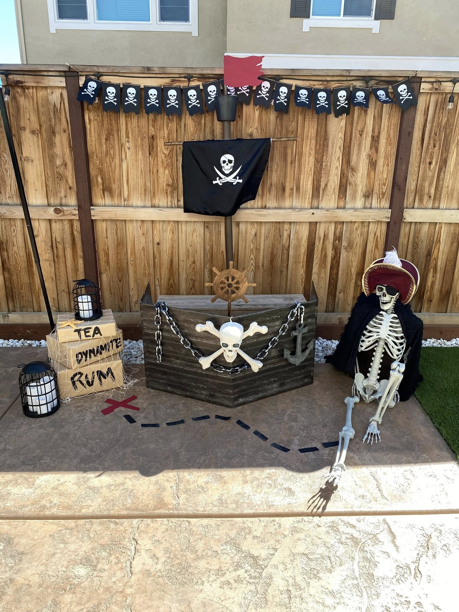 DIY outdoor pirate ship Halloween decoration scene with a skeleton pirate, skull and crossbones flag, and prop crates.