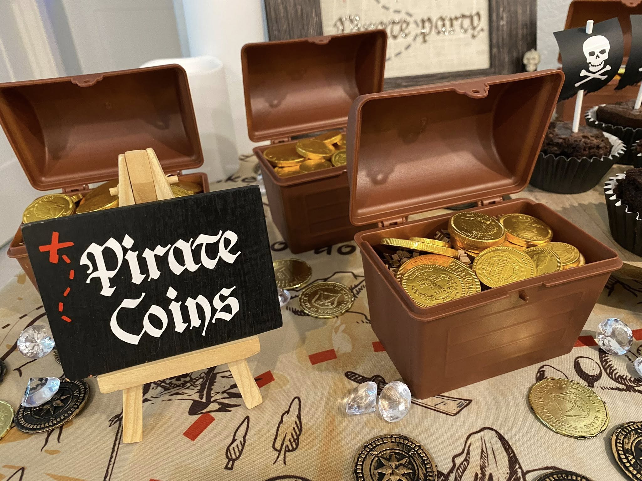 Small brown treasure chests filled with gold pirate coins on a treasure map tablecloth