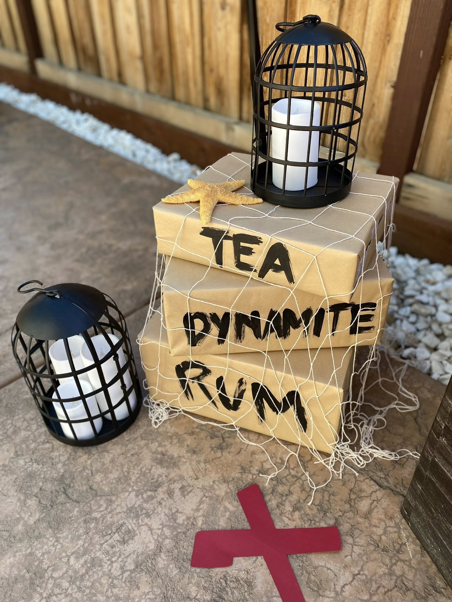 Nautical themed party decoration with stacked kraft paper boxes labeled TEA, DYNAMITE, and RUM draped in fishing net.
