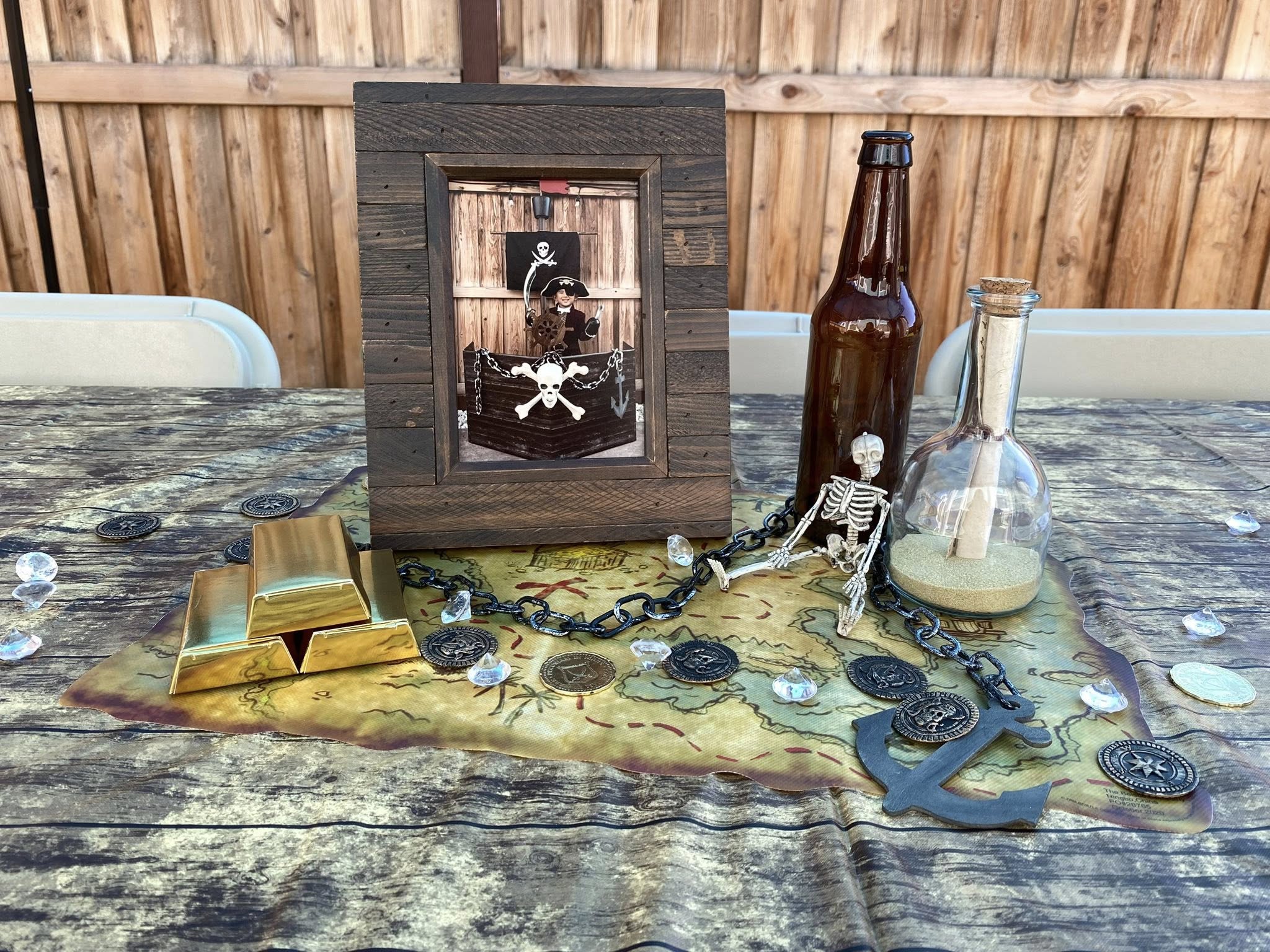 Pirate-themed party table centerpiece with a picture frame, gold bars, skeleton figurine, and a message in a bottle.