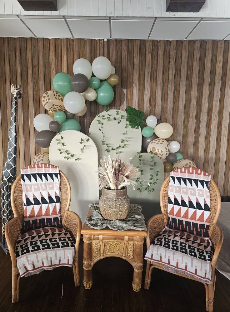Boho safari-themed party backdrop with wicker chairs, arched panels, and balloon garland.