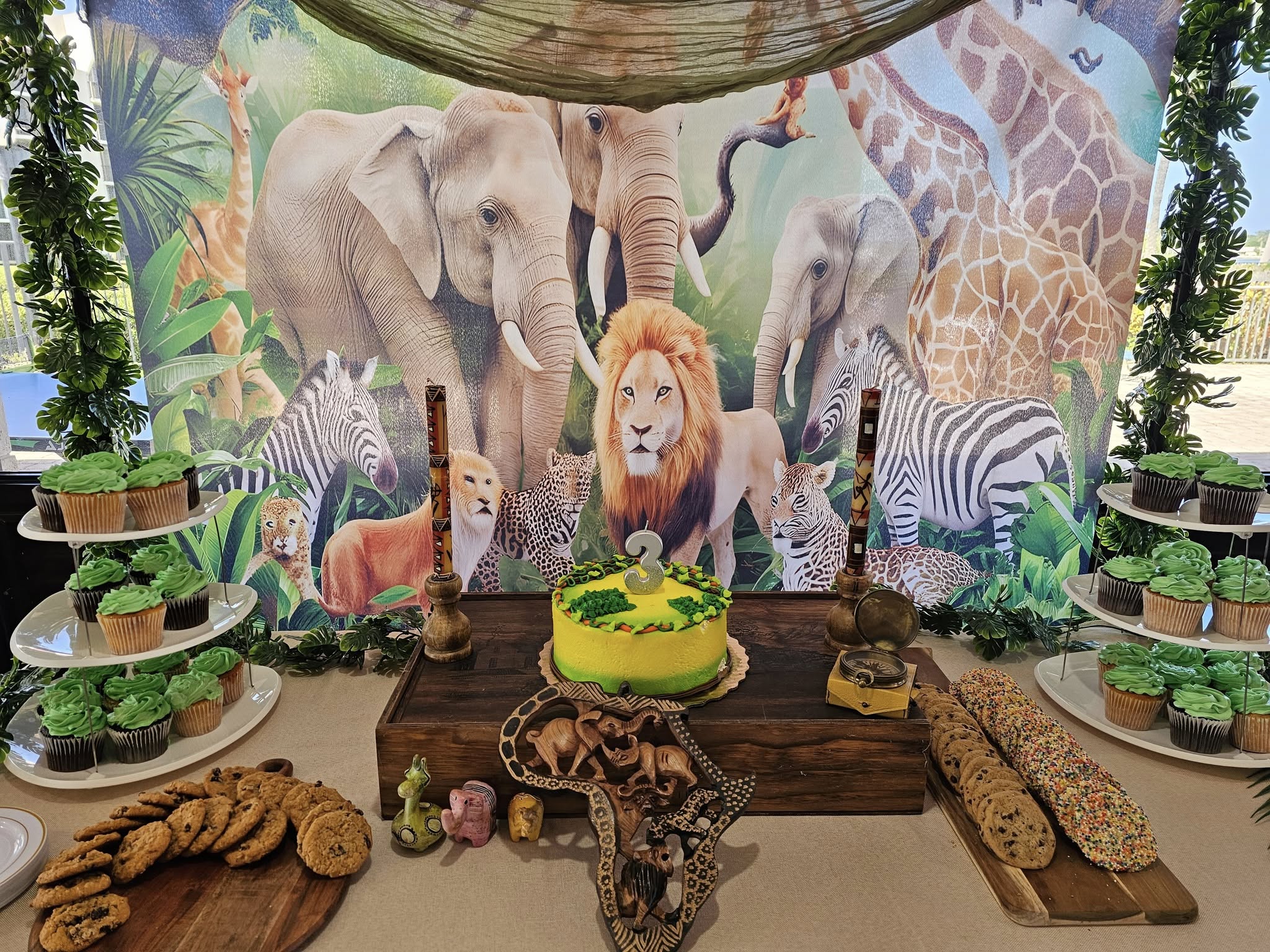 Jungle-themed birthday display with a cake featuring a number 3 topper, surrounded by animal-themed decorations.