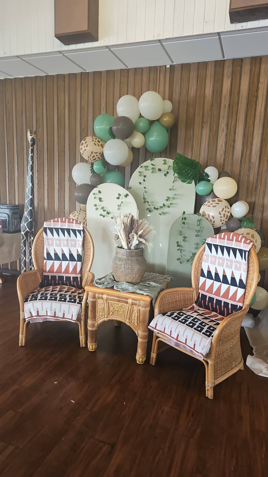 Safari themed event decor with bamboo chairs, mudcloth patterned blankets, balloons, and decorative backdrops.