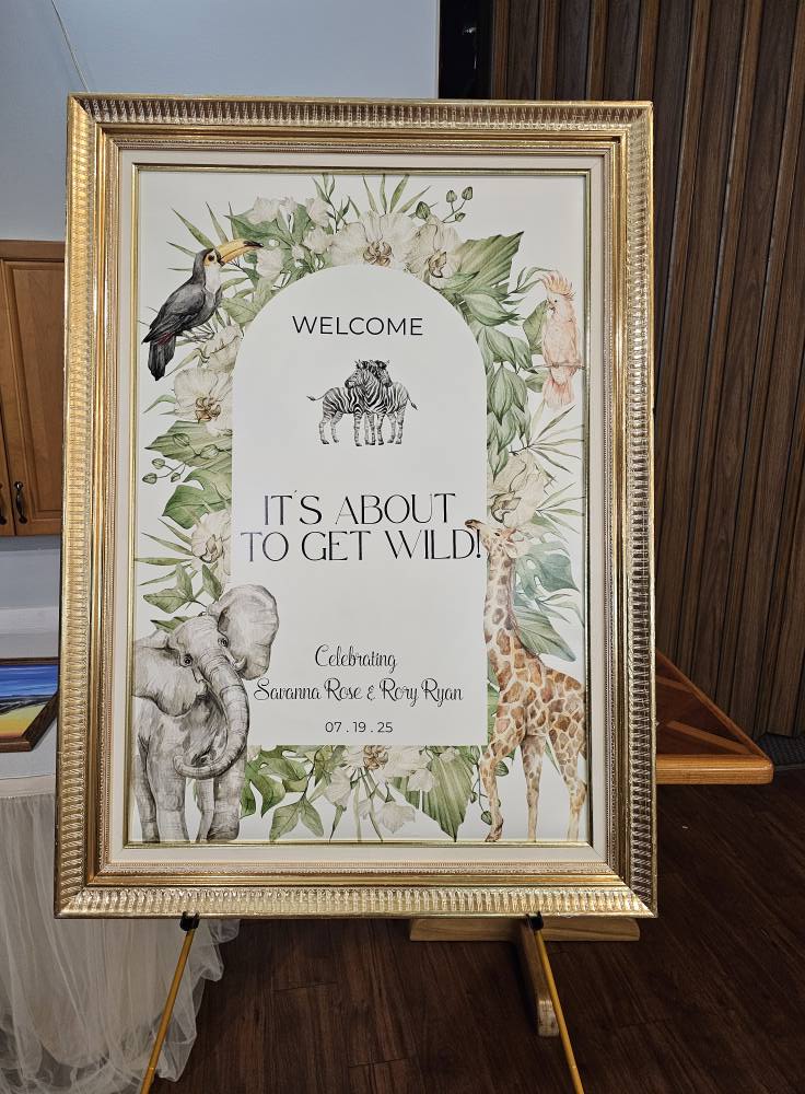 Framed gold sign featuring a jungle theme with safari animals, text reading Welcome, It's About To Get Wild, and the names Savanna Rose and Rory Ryan with the date 07.19.25.
