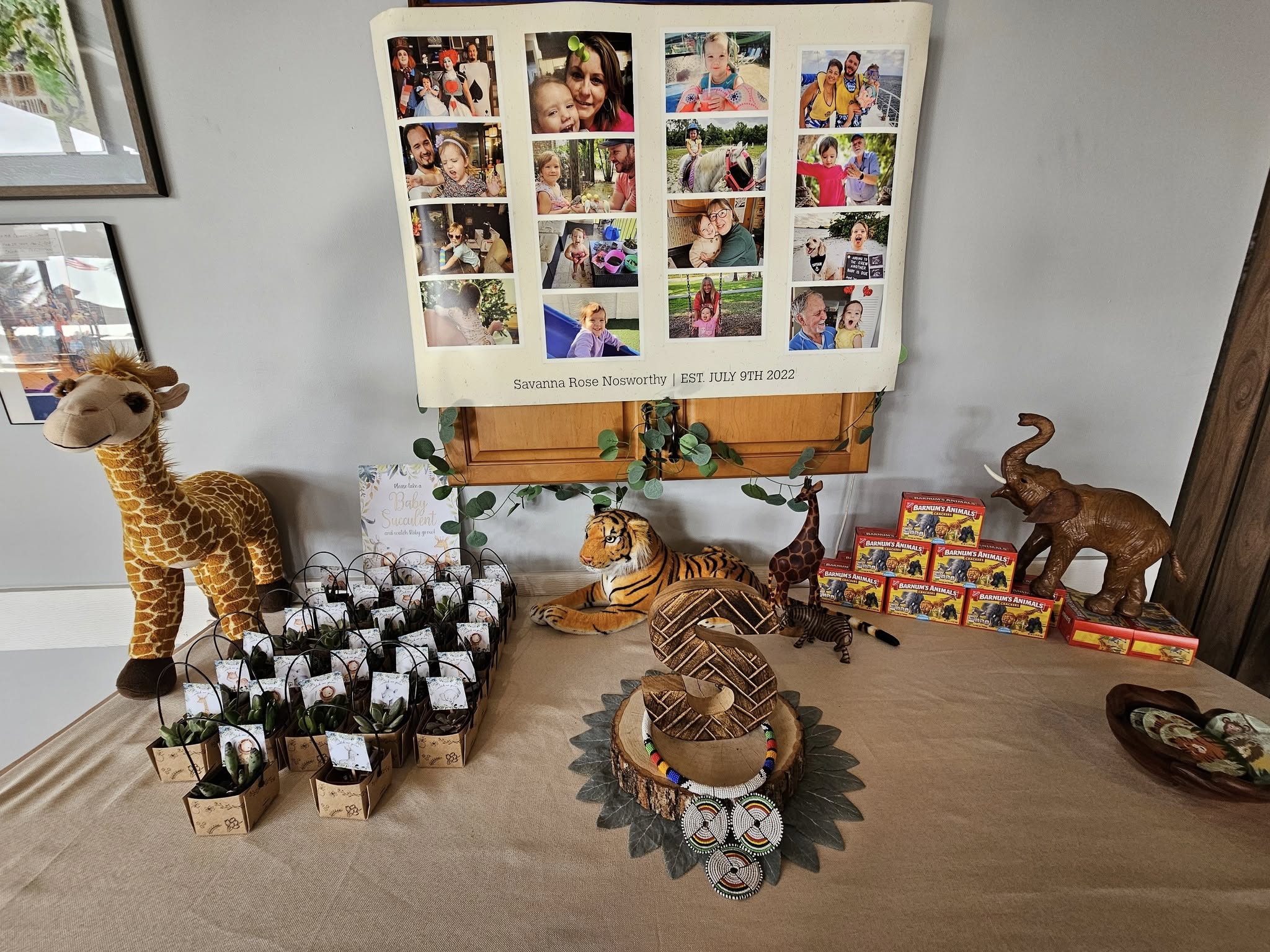 Safari-themed party table featuring a photo collage, plush animals, and succulent favors.