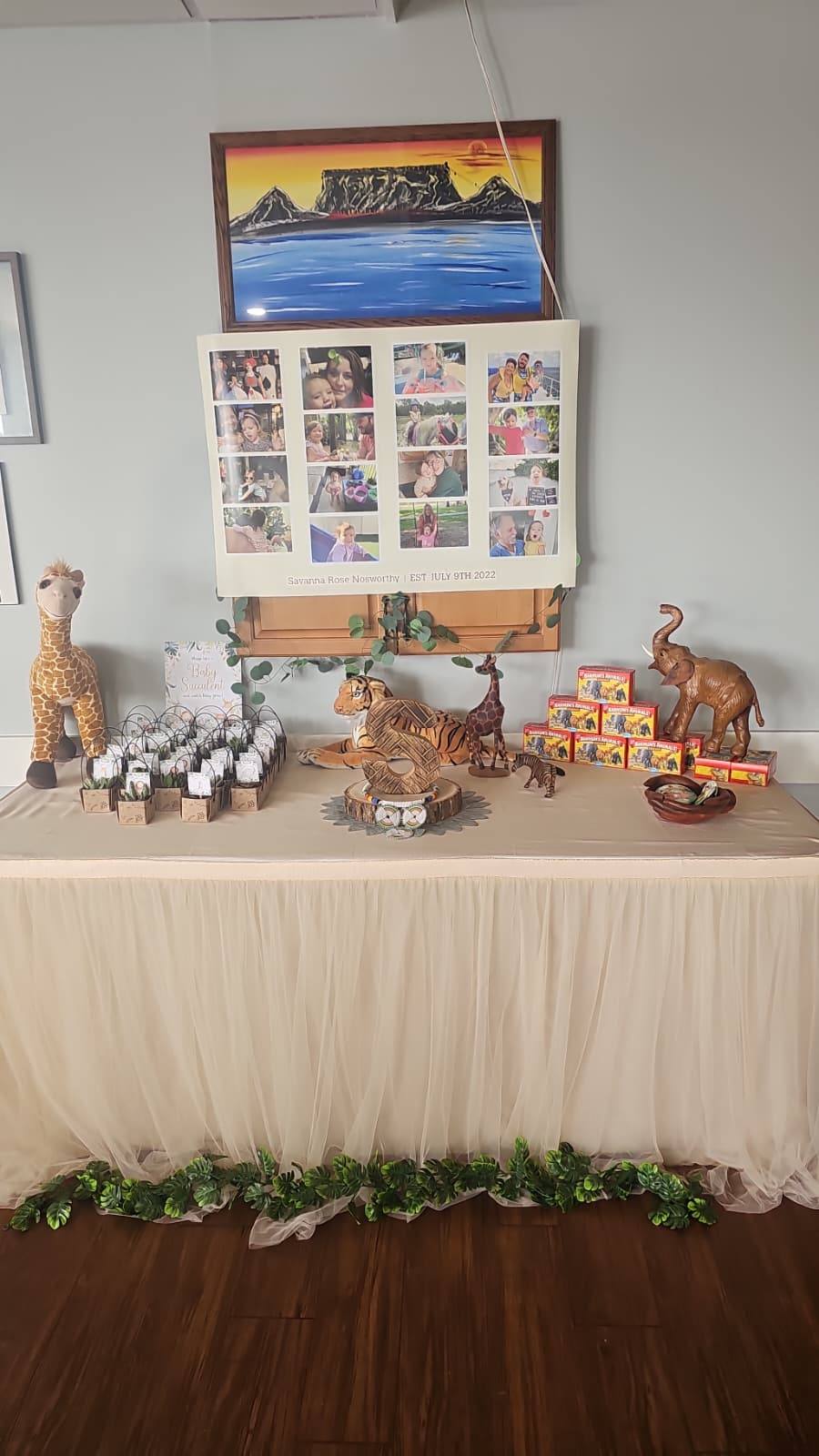 Safari-themed party table featuring a photo collage, wooden letter S, animal figurines, and succulent party favors.