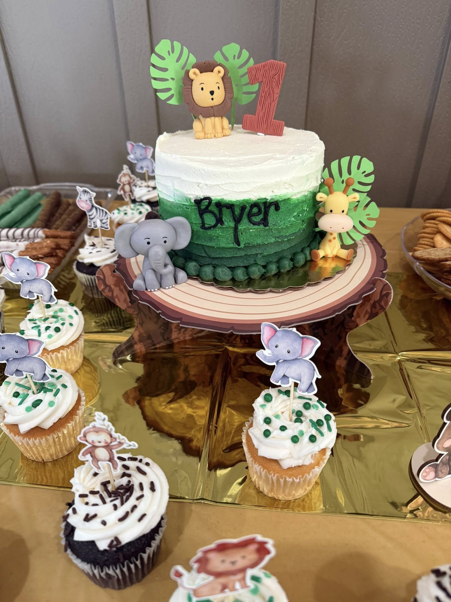 Jungle-themed first birthday cake with animal toppers and matching safari cupcakes