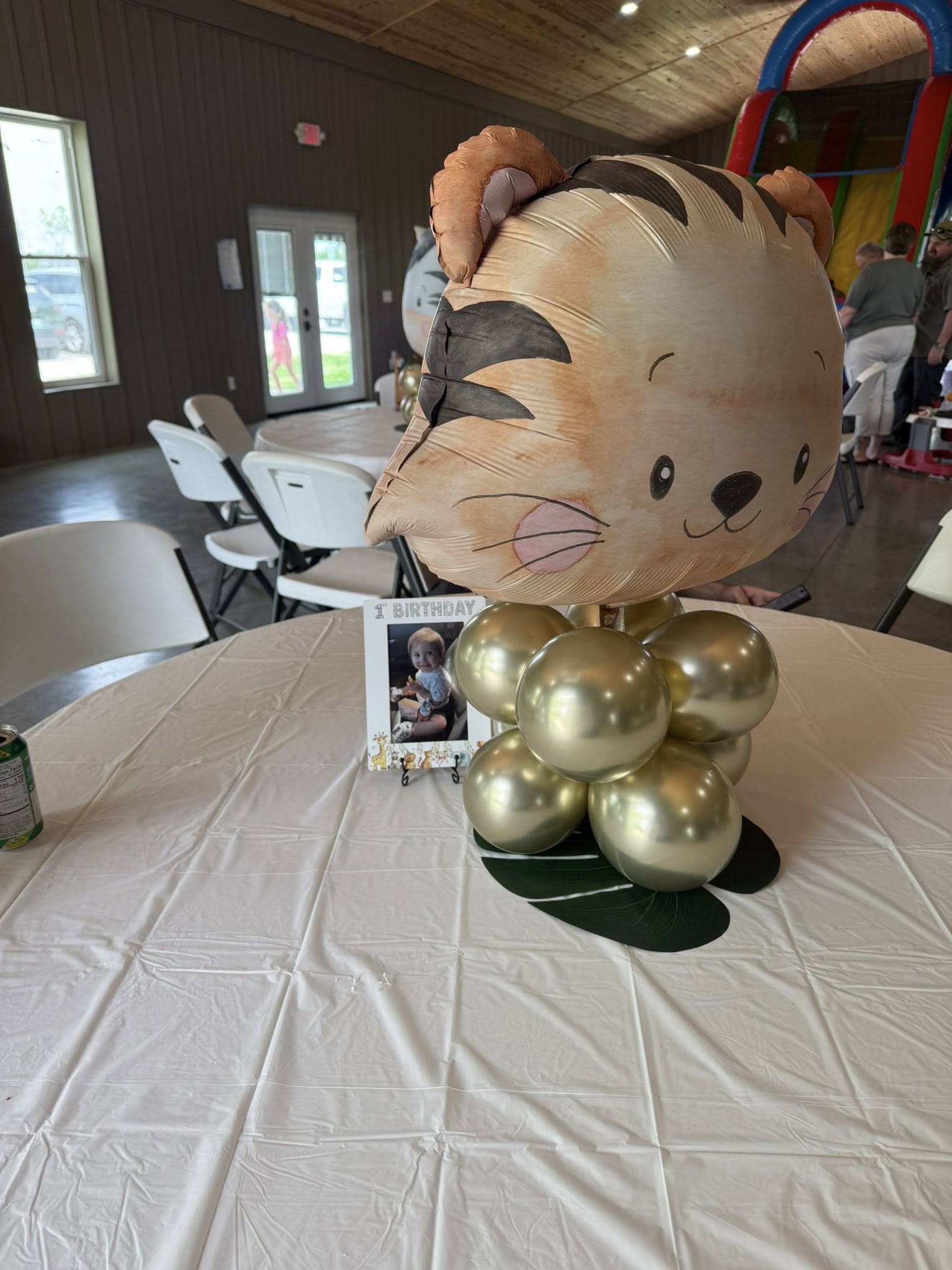 Tiger-themed balloon centerpiece with a 1st birthday photo frame on a table.