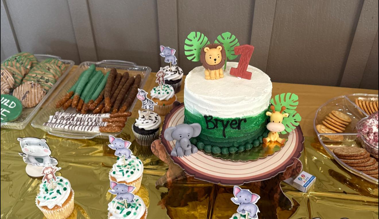 Jungle-themed first birthday cake with animal toppers and matching giraffe and elephant cupcakes.
