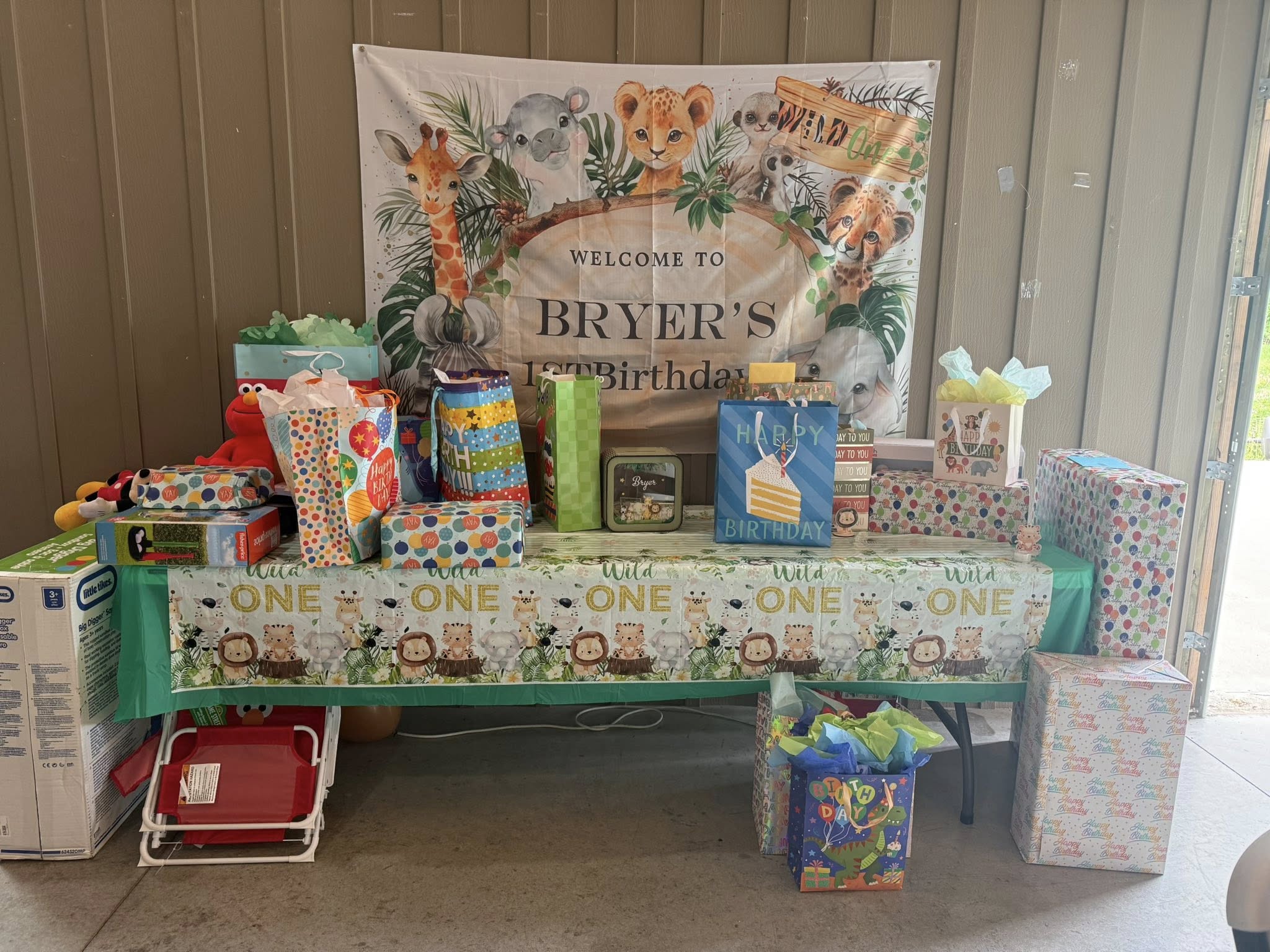 Birthday party table decorated with a jungle-themed banner saying Bryer's 1st Birthday and wrapped gifts.