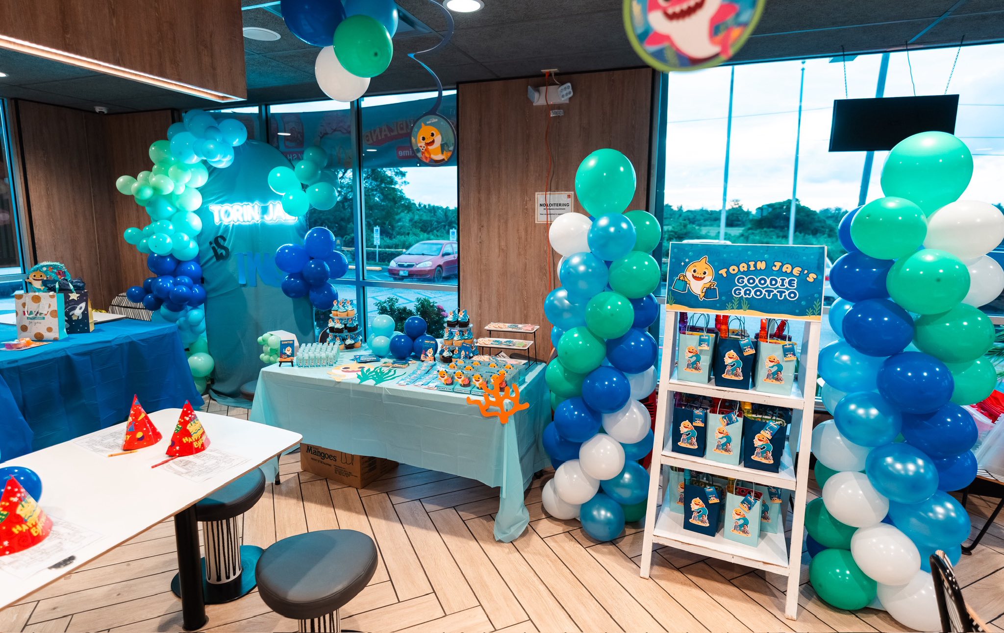 Baby Shark themed birthday party setup with a goodie bag shelf and balloon pillars in shades of blue and green.