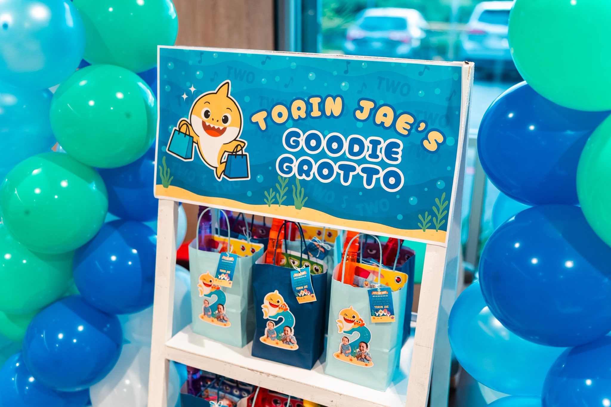 Display sign labeled Torin Jae's Goodie Grotto surrounded by blue and green balloons alongside birthday gift bags.