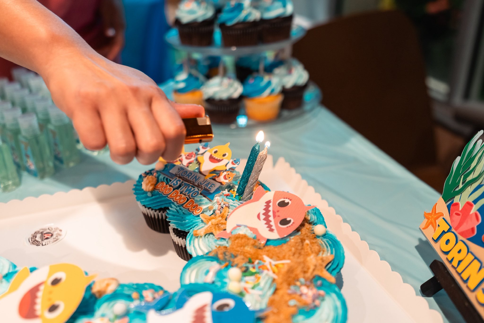 Hand lighting two candles on a Baby Shark-themed pull-apart cupcake cake for a second birthday.