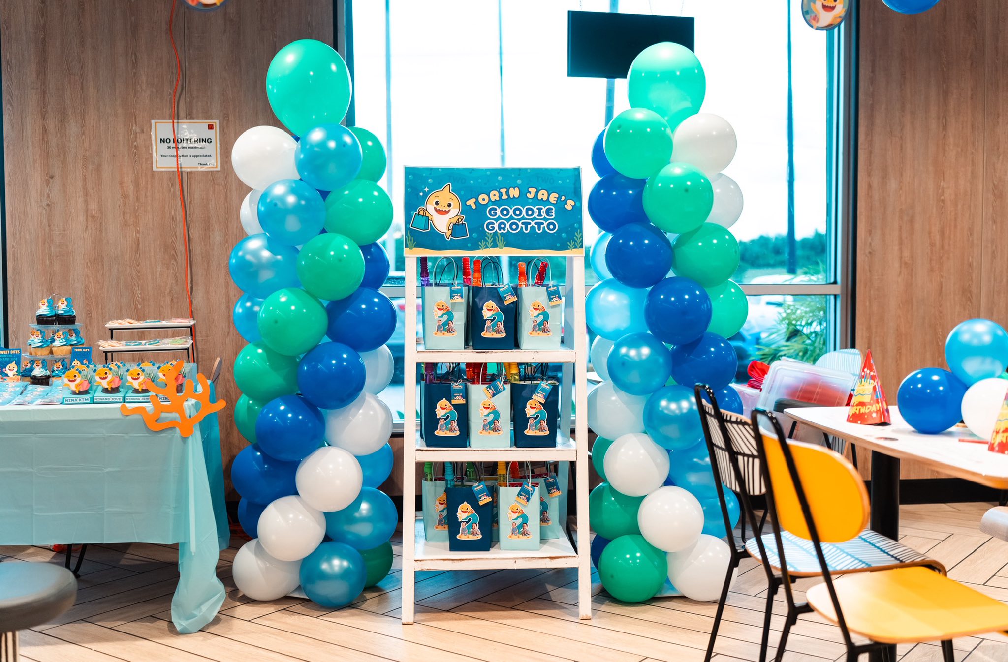 Baby Shark themed birthday goodie bag display stand flanked by blue and white balloon columns.