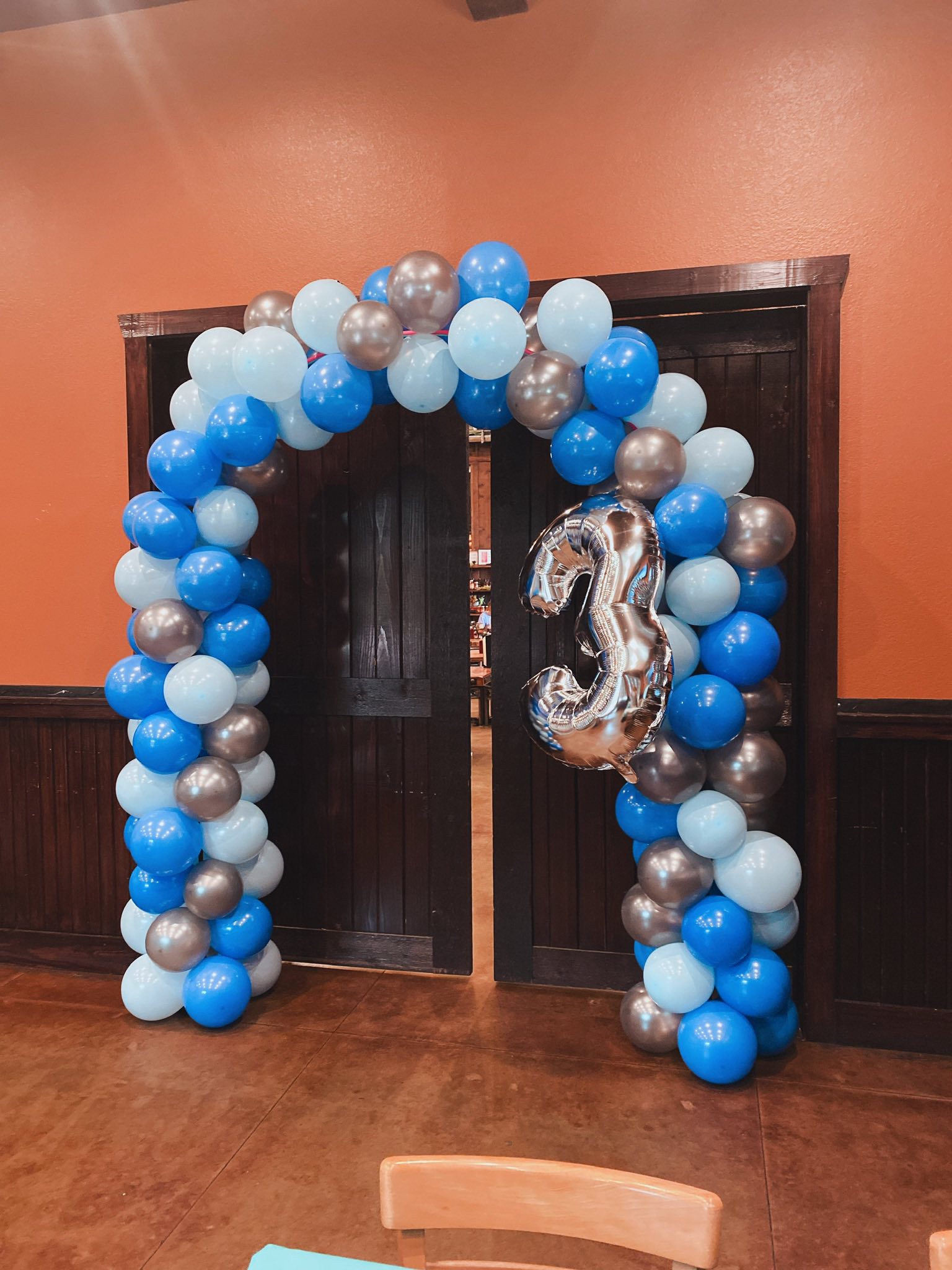 Blue and silver balloon arch surrounding a doorway with a large silver number 3 balloon.