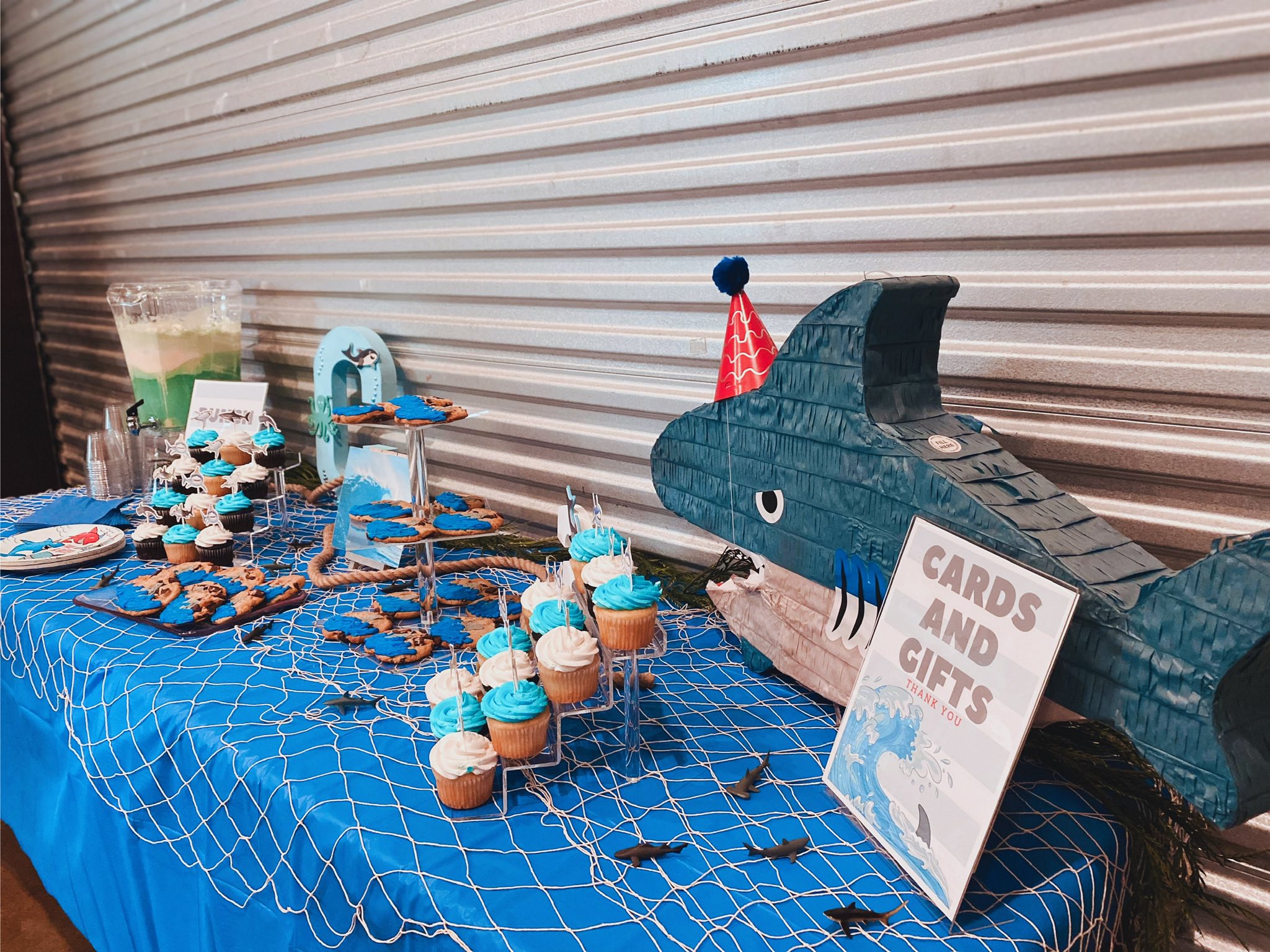Shark-themed dessert table with cupcakes, cookies, and a cards and gifts sign at a birthday party.