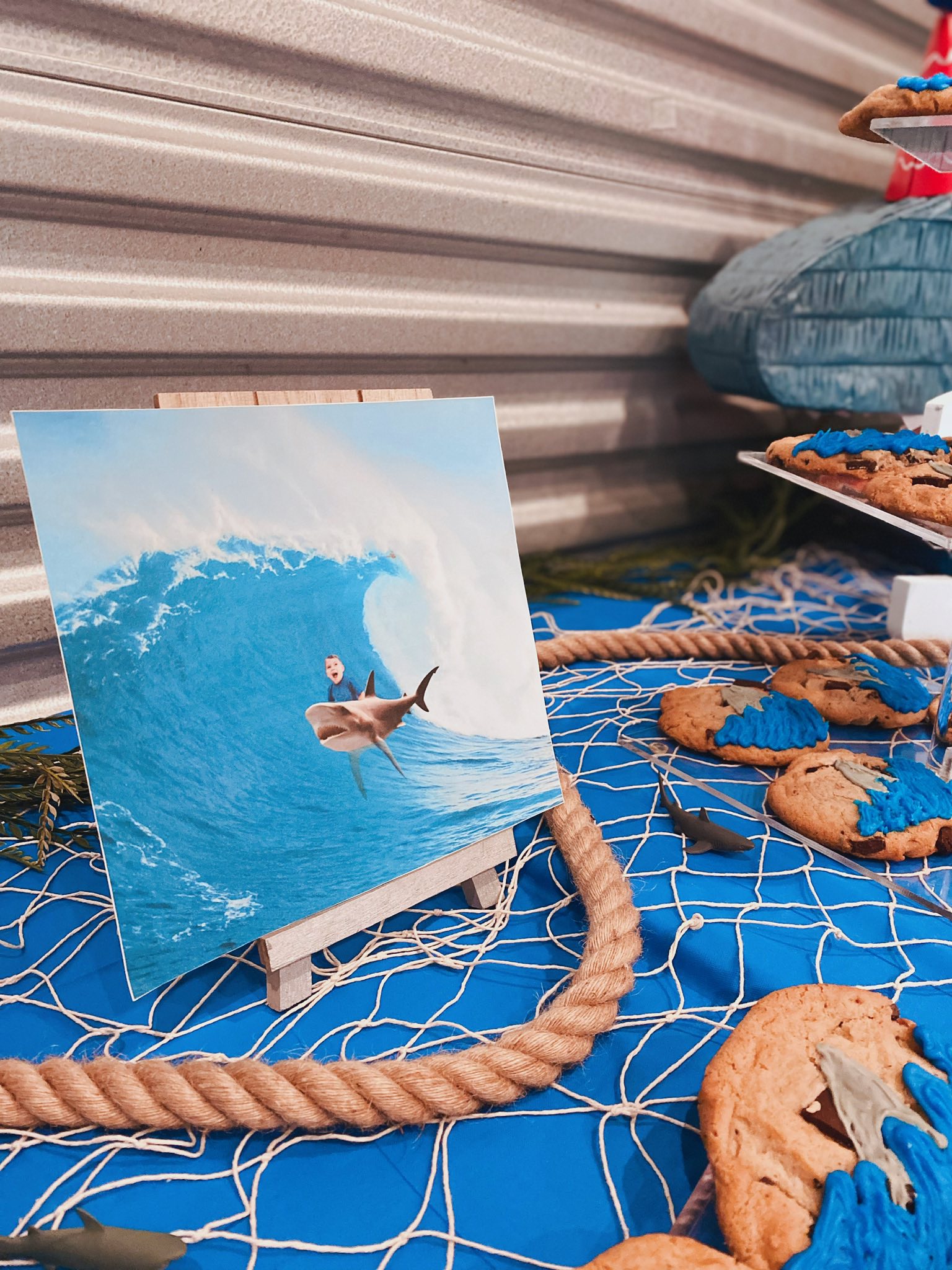 Photo on display showing a young boy riding a shark on a large ocean wave at a shark-themed party