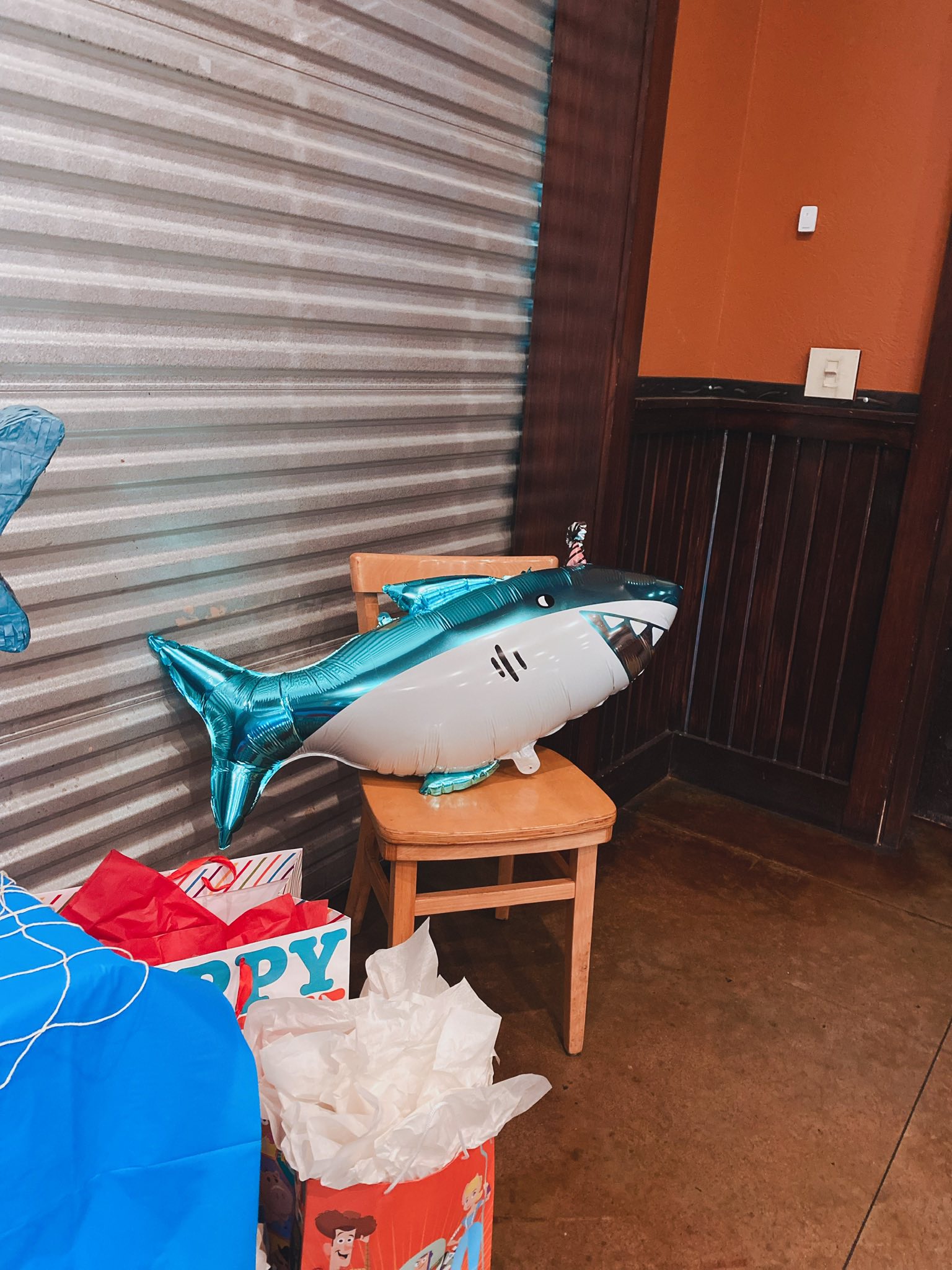 Shiny blue shark-shaped party balloon resting on a wooden chair.