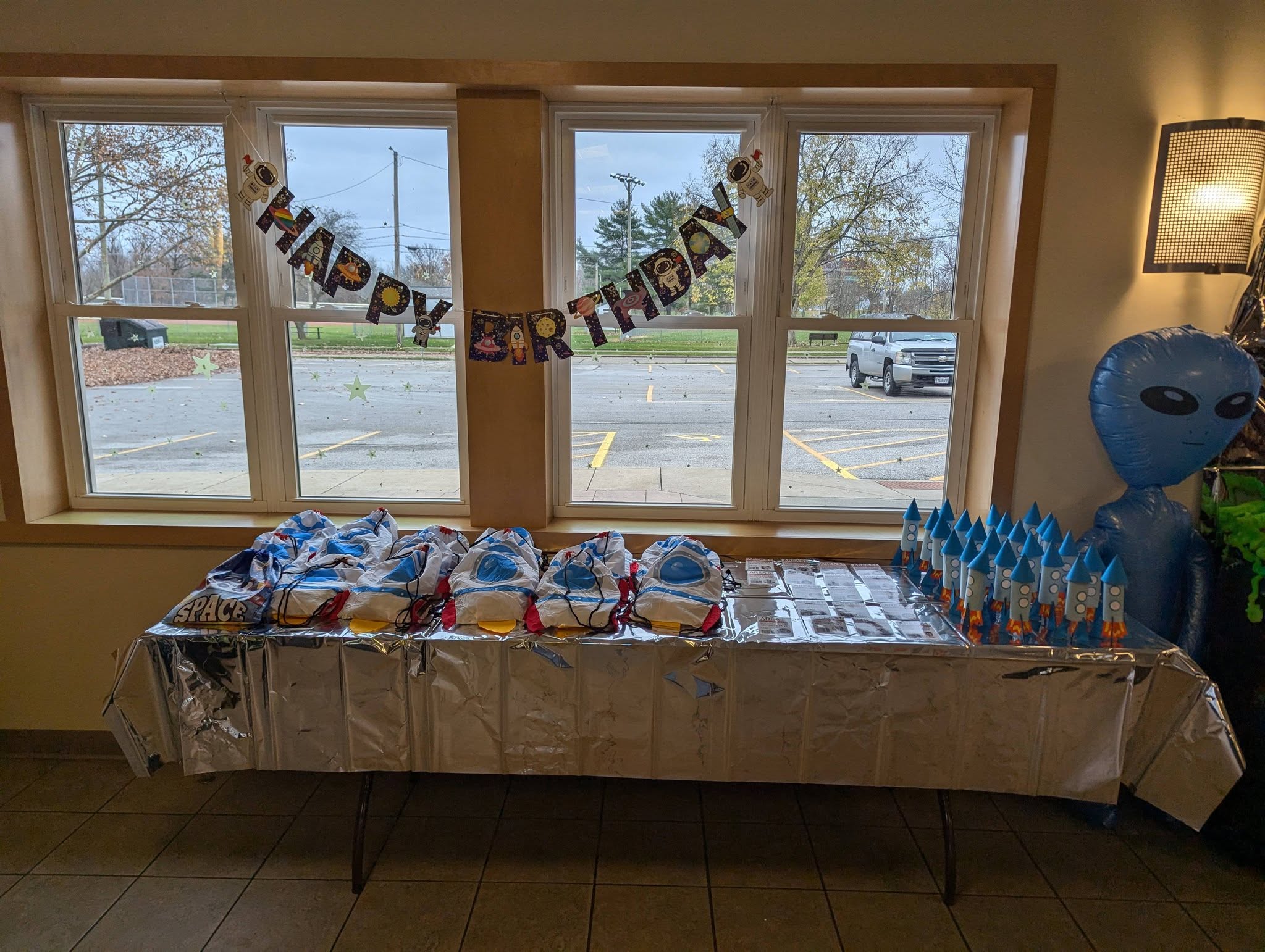Space themed birthday party table with party favor bags, rocket centerpieces, and an inflatable alien balloon.