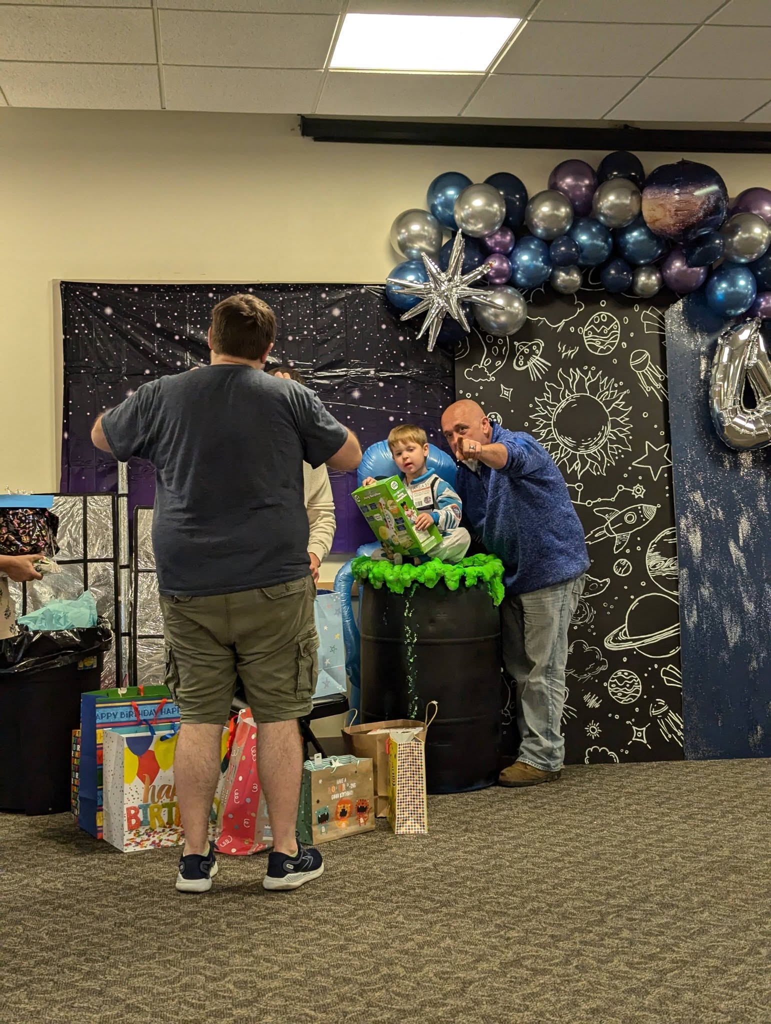 Toddler in astronaut costume sitting by space-themed birthday decor with family