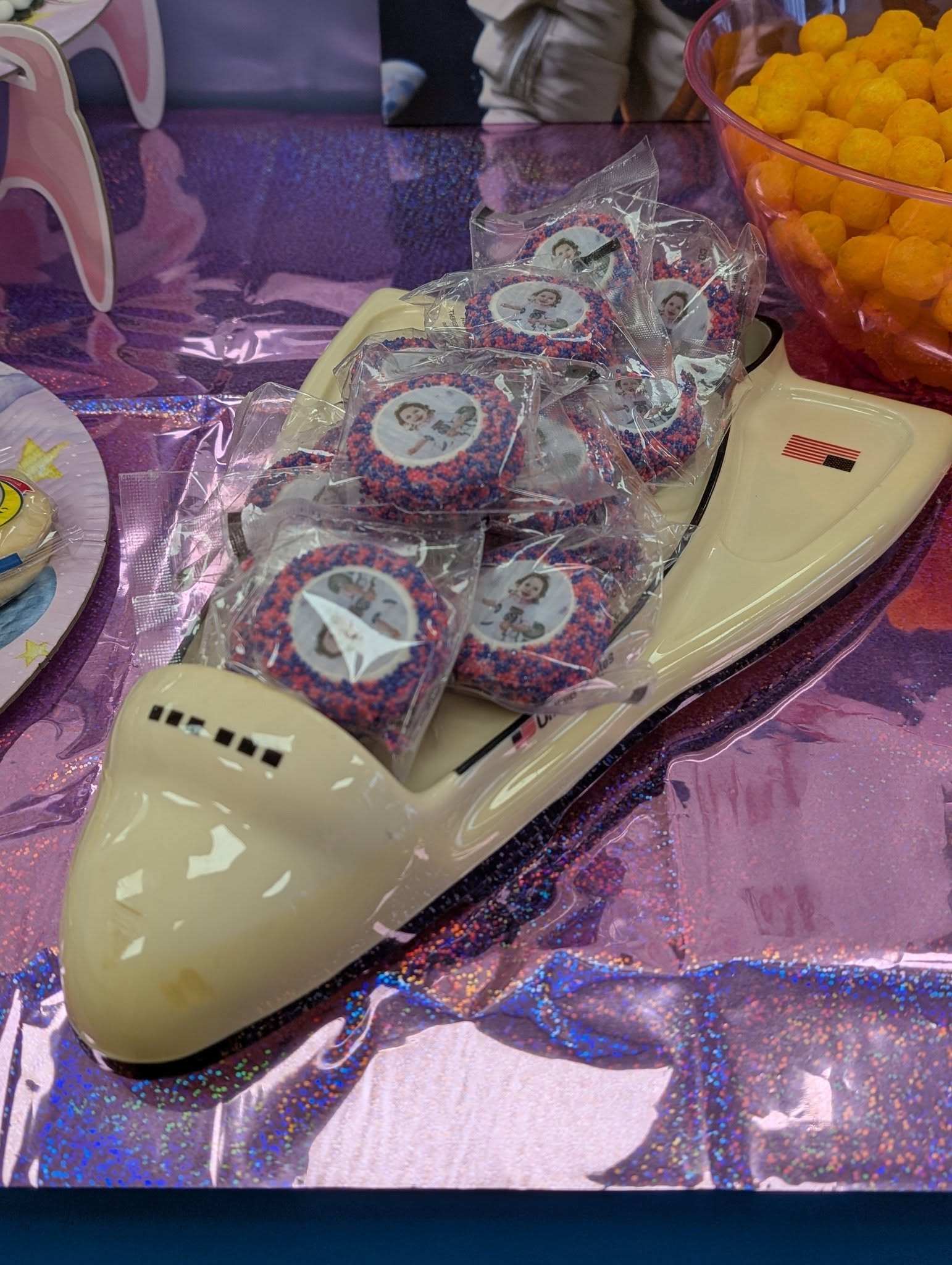 Space shuttle serving tray filled with individually wrapped sprinkle-covered cookies featuring custom photos.