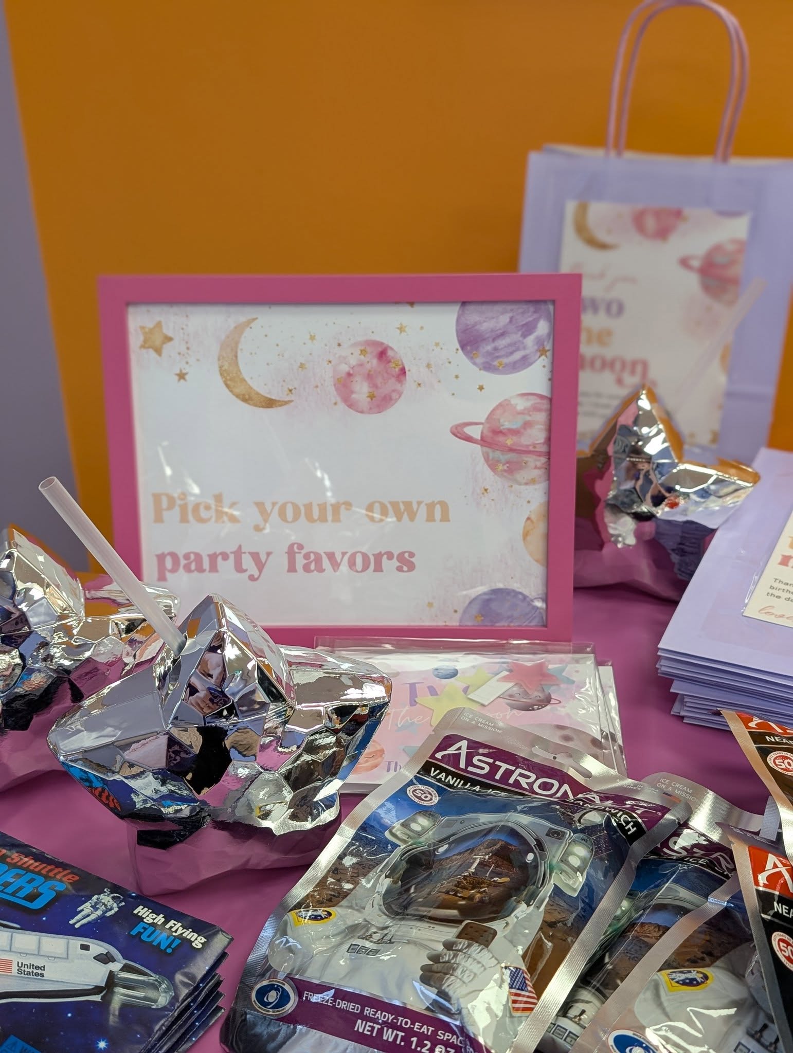 Table display featuring a sign that reads Pick your own party favors surrounded by astronaut-themed treat bags.