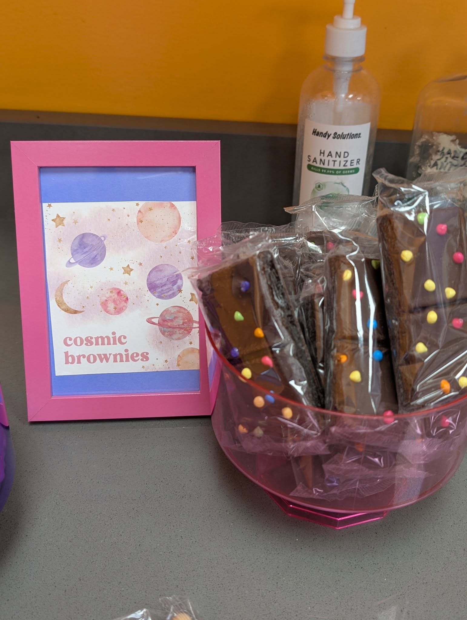 Bowl of individually wrapped cosmic brownies next to a framed sign
