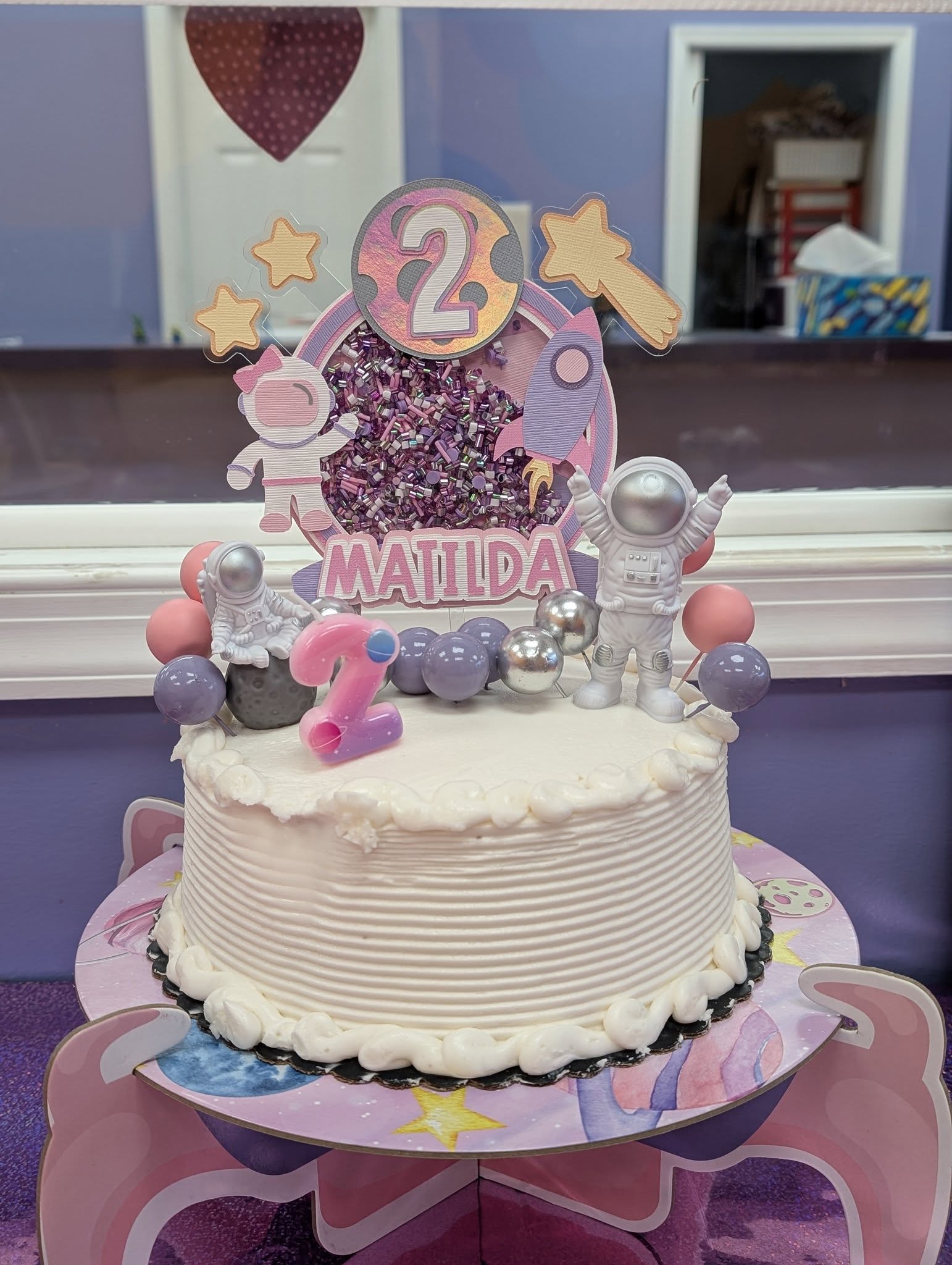 Space-themed cake topper set reading Matilda with a number 2 centerpiece, astronaut figures, and stars.