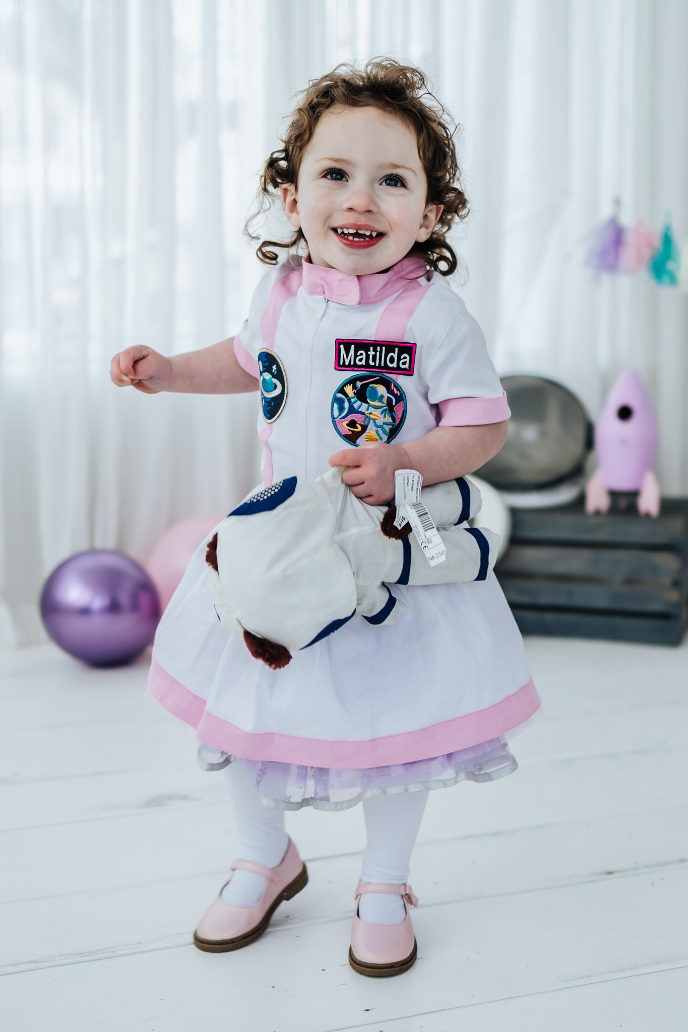 Toddler smiling while wearing a pink and white personalized astronaut costume.