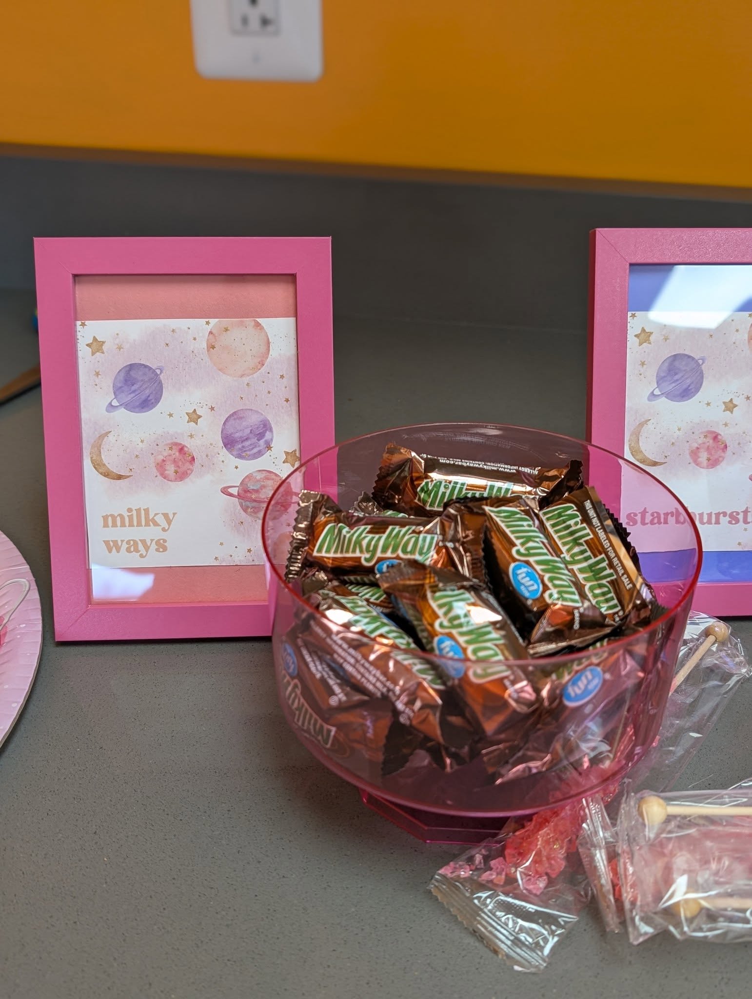 Bowl of Milky Way fun size candy bars next to a framed space-themed sign labeled milky ways.