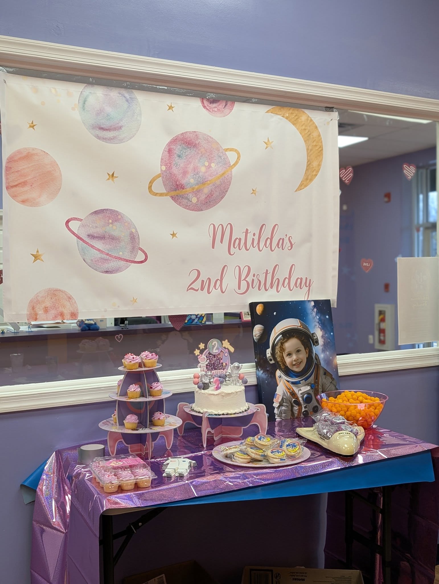 Space-themed birthday party table with a cake, cupcakes, and photo of a child in an astronaut costume.